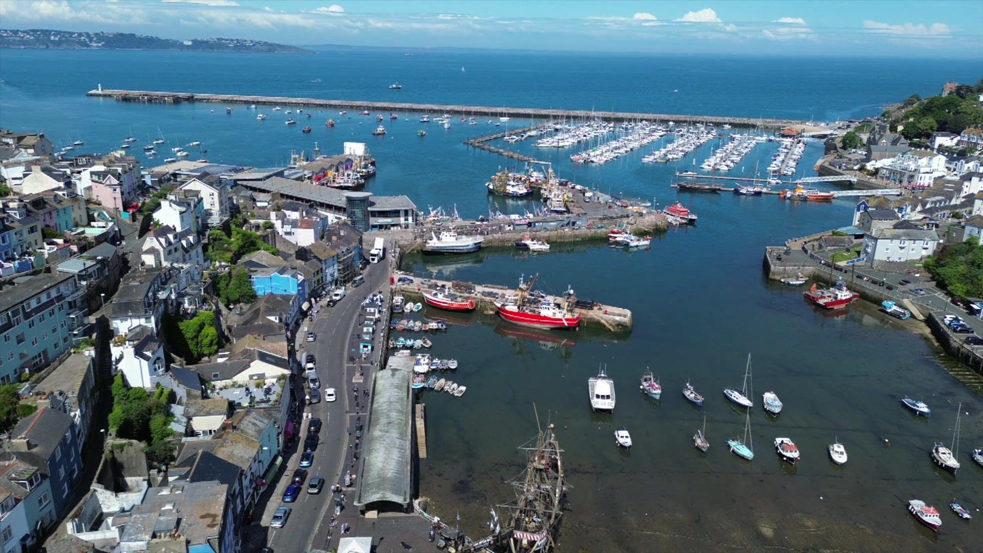 An aerial shot of a harbour with a large number of boats in a marina and a town on the left with roads and houses.