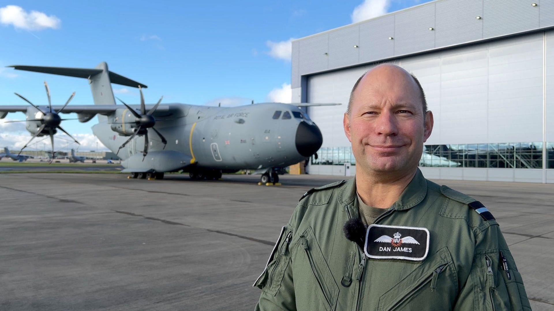 Air Commodore Dan James in his flight suit stands in front of the plane outside a hangar.