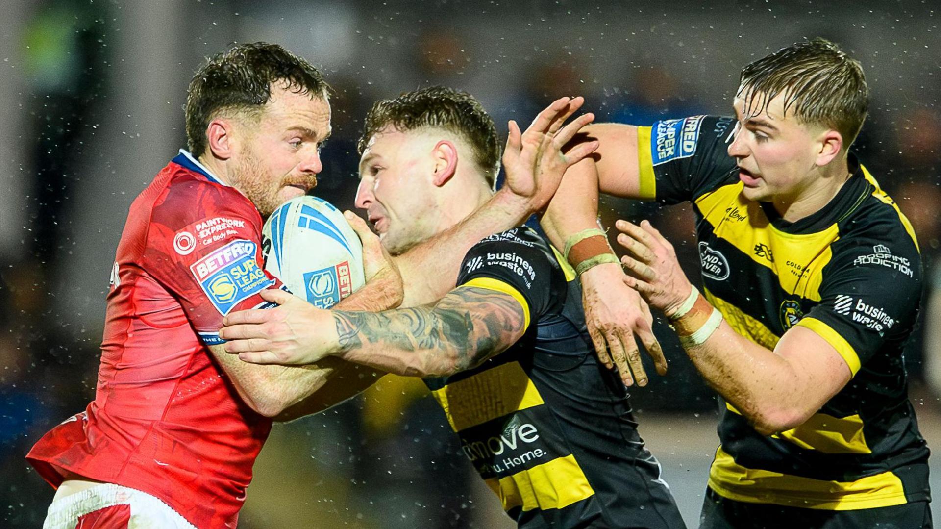 Hull KR winger Joe Burgess (left), with the ball under his right arm, is held up and tackled by York duo Liam Harris (centre) and Oli Field (right)