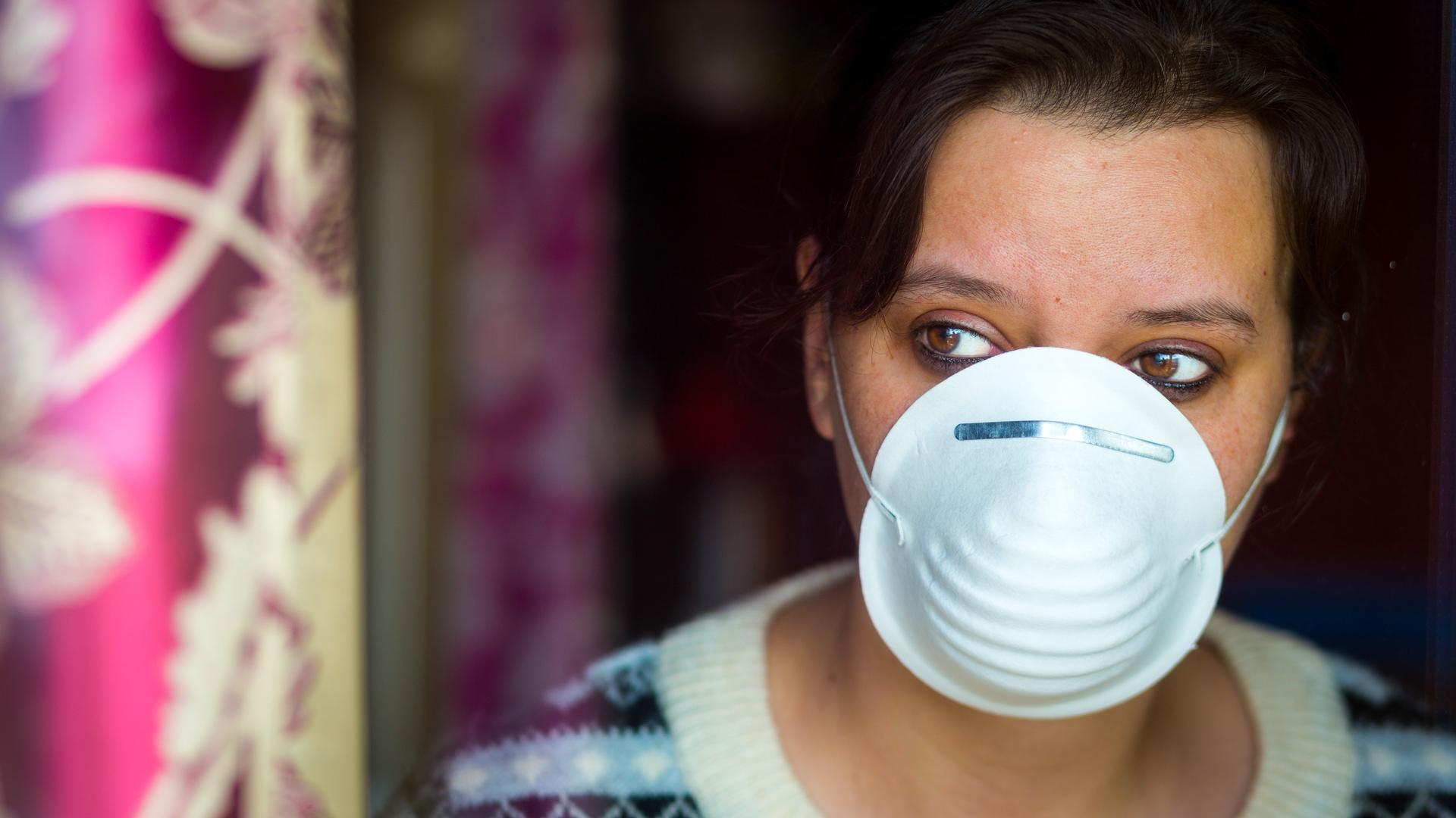 Woman wearing a face mask looks out of a window