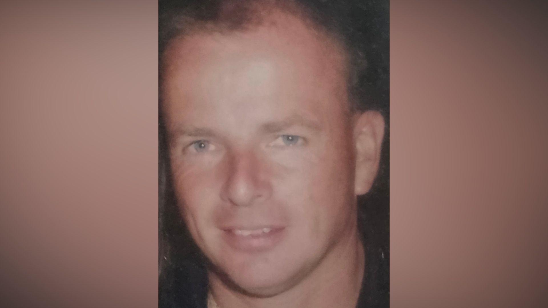 A man with dark hair smiles at the camera. He is wearing a black top. 
