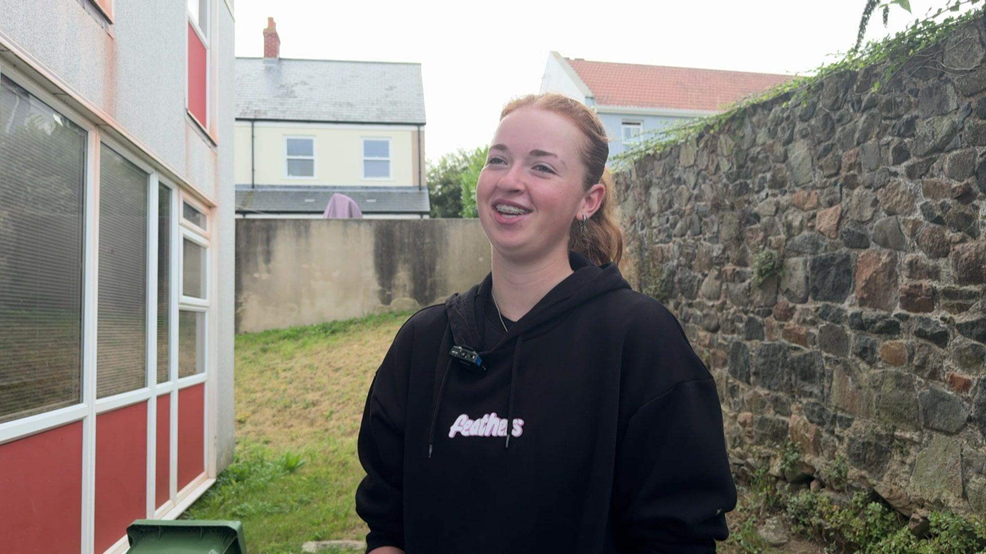 Tilly smiling and wearing a dark hoodie with the word 'feathers' written on it. Tilly's hair is pulled back into a ponytail.