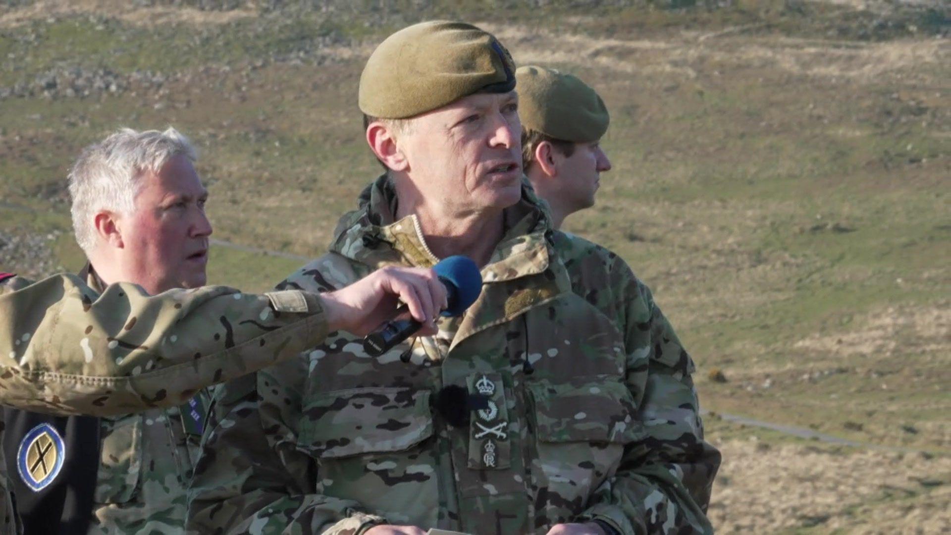 General Sir Roland Walker, chief of the general staff for the British Army. He is speaking into a microphone on the moors, with other military personnel around him.