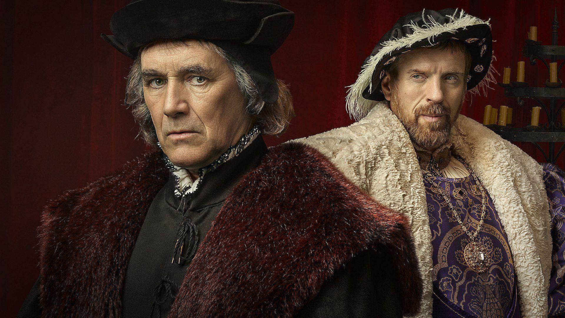 A promotional image for the Wolf Hall series. To the right is Mark Rylance as Thomas Cromwell in period costume with a black hat and top and a claret fur cloak.  To the left is Damian Lewis dressed as King Henry VIII with a feathered hat, white cape and purple tunic.