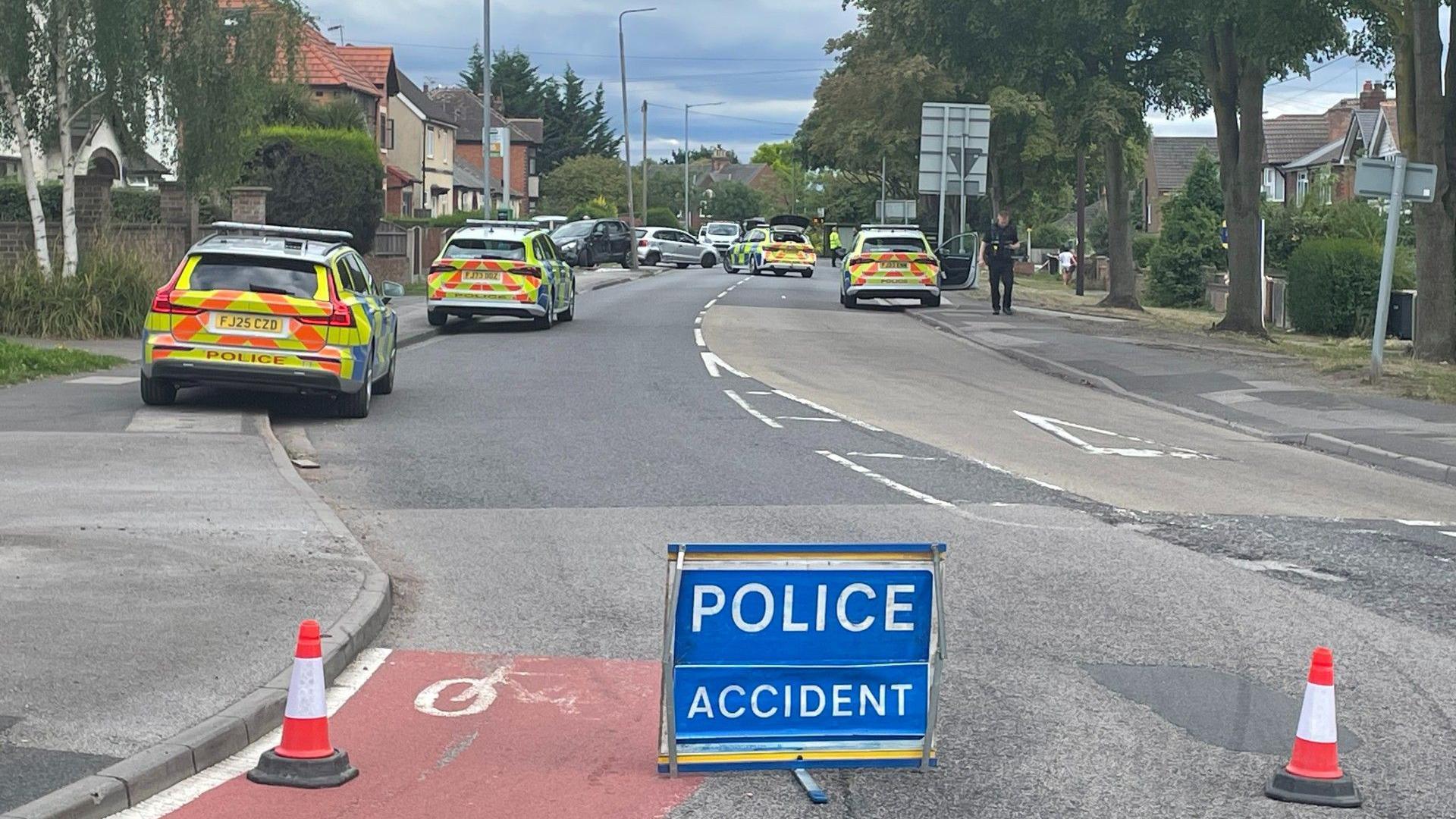 Residential road with four police cars parked along it and a police warning sign in foreground
