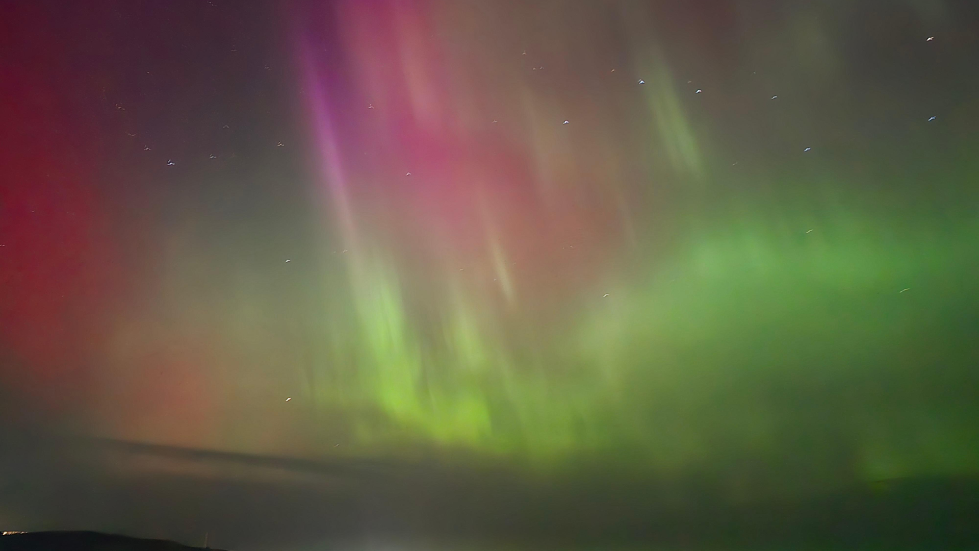 View of the night sky illuminated in hues of red, pink and green from the aurora borealis