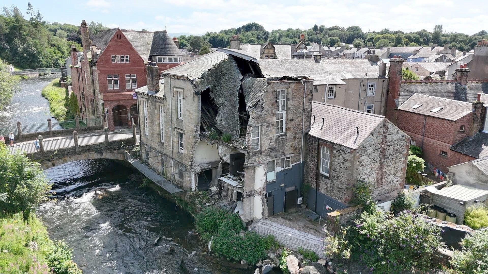 View of the rear of the Old Courthouse. A large section of the stone-built property is missing. It is next to the River Cocker and Cocker Bridge.