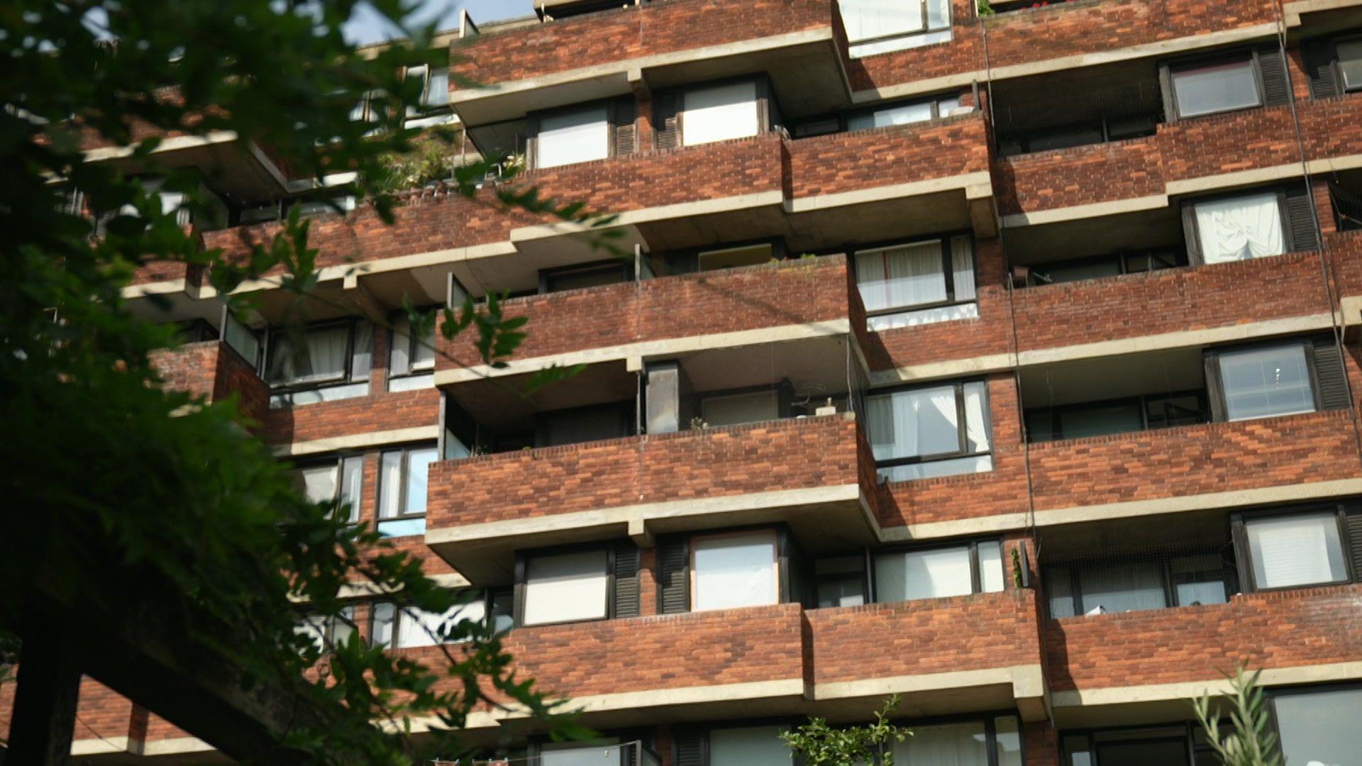 An exterior view of a block of flats made with red brick. There are balconies for each one. 
