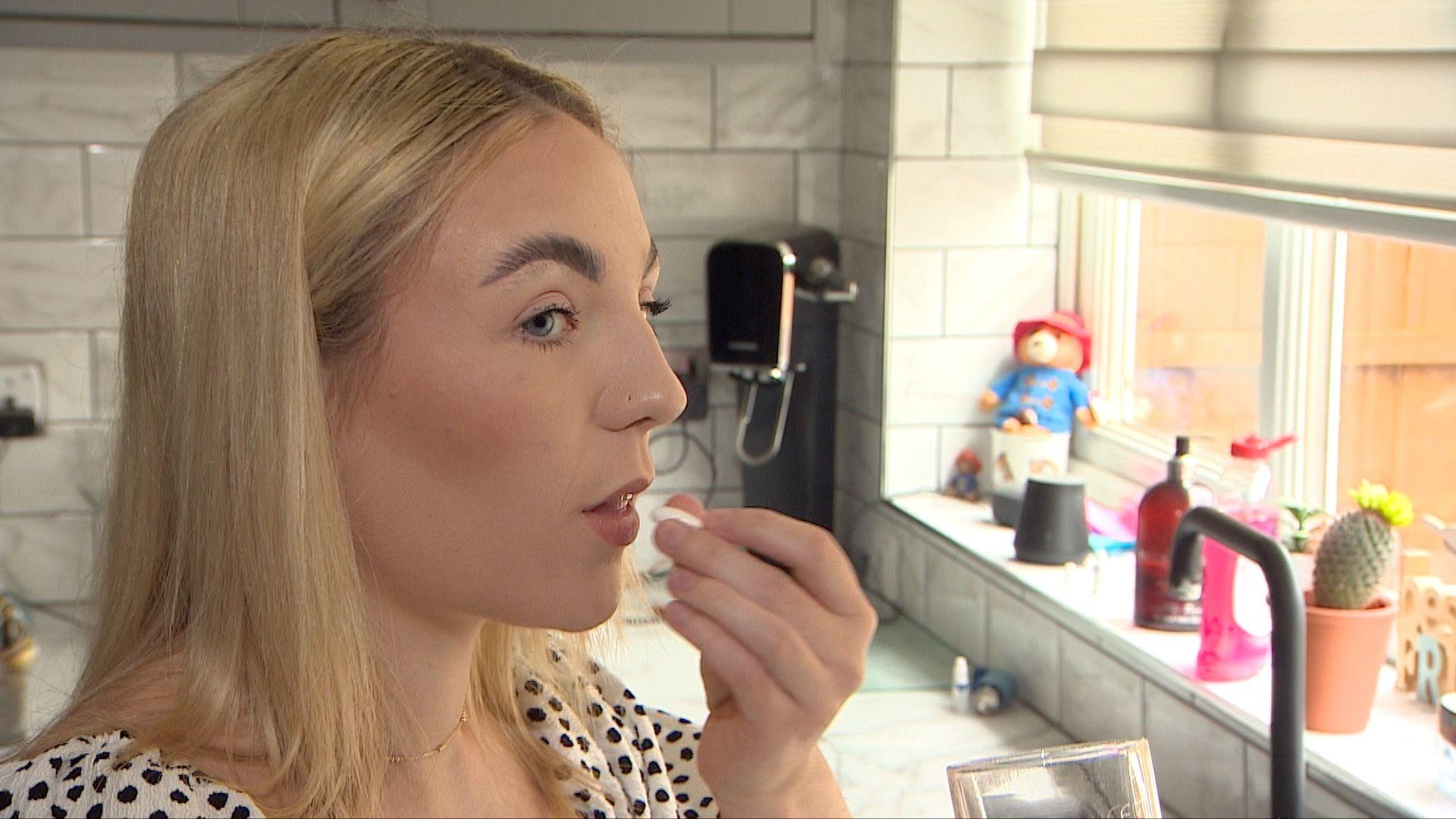 Gemma Cutler taking an over-the-counter painkiller in a kitchen