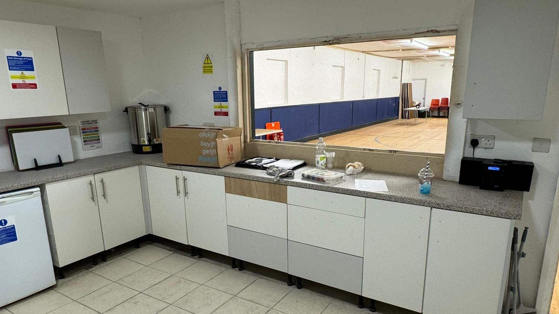 A new kitchen with white cupboards and a hatch with opens onto a hall with a pine floor 