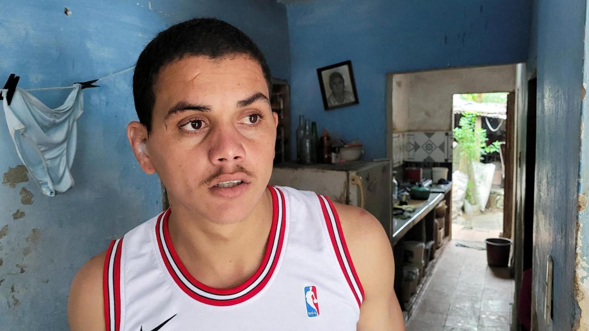 Dariel Cruz García, wearing a white basketball shirt, poses for a photo at his home in Havana, Cuba, after being released from prison