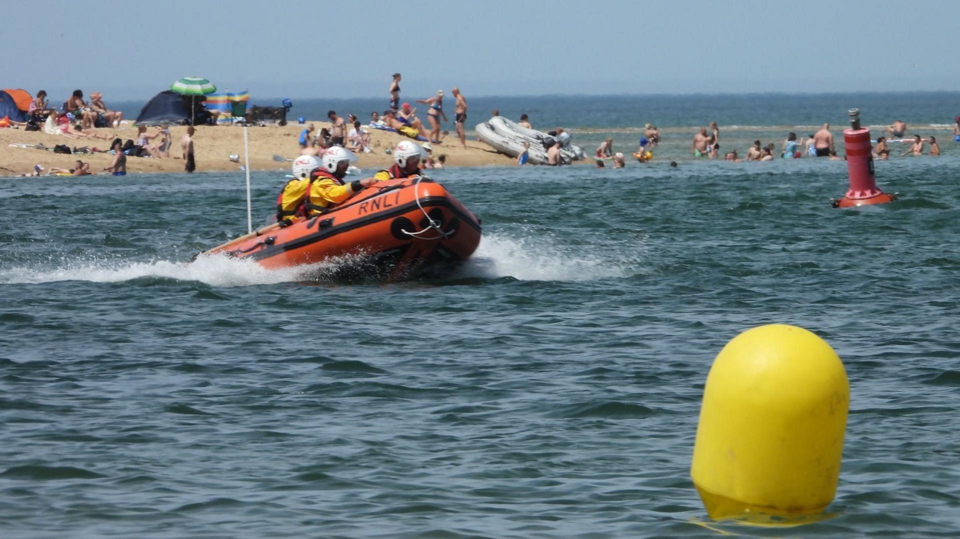 A RNLI orange lifeboat in the sea with three visible crew members on board.