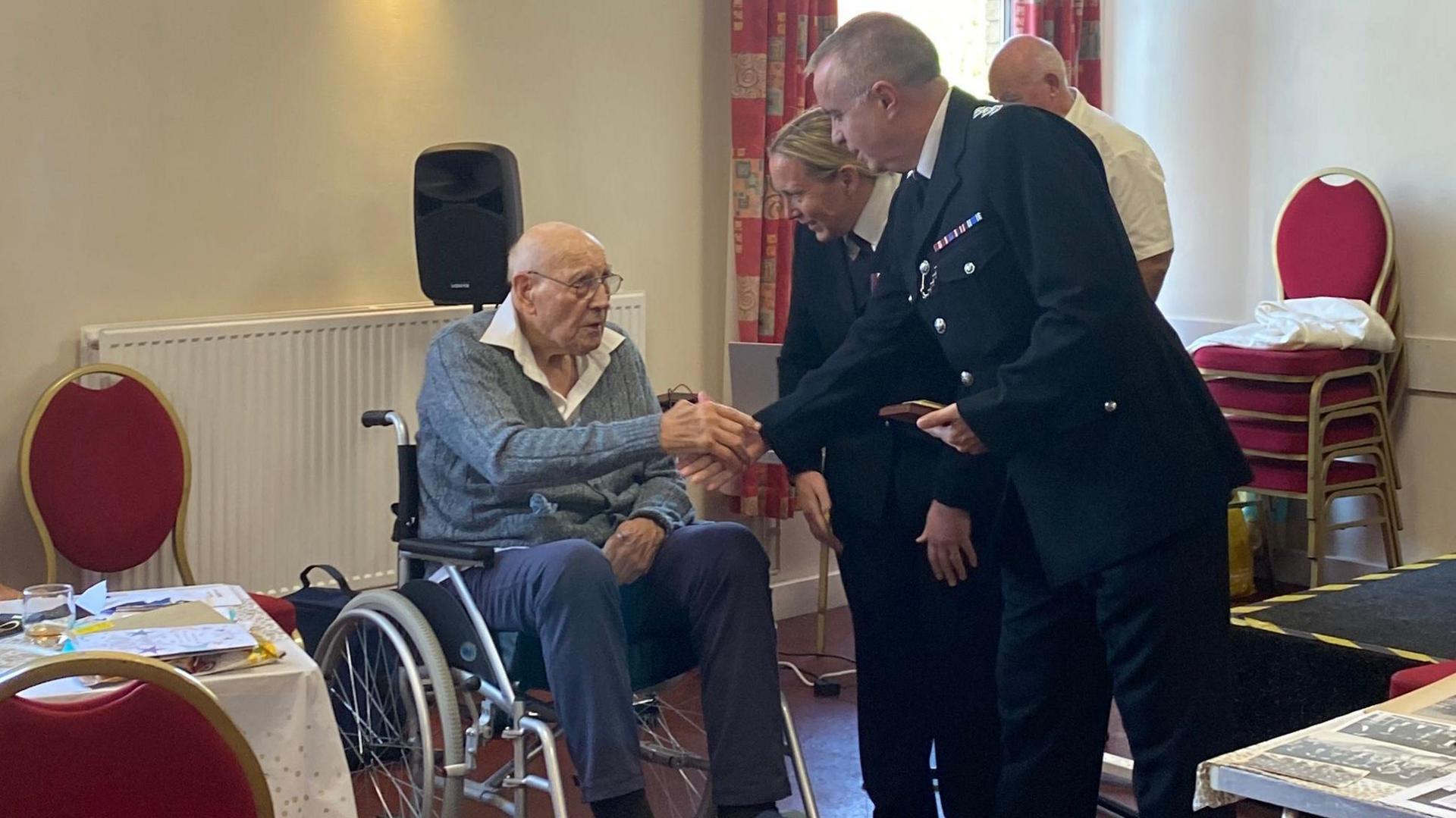 Eric Birkin, in a wheelchair, shacking hands with Det Ch Insp Rob Huddleston, with Ch Supt Claire Talbot standing behind him