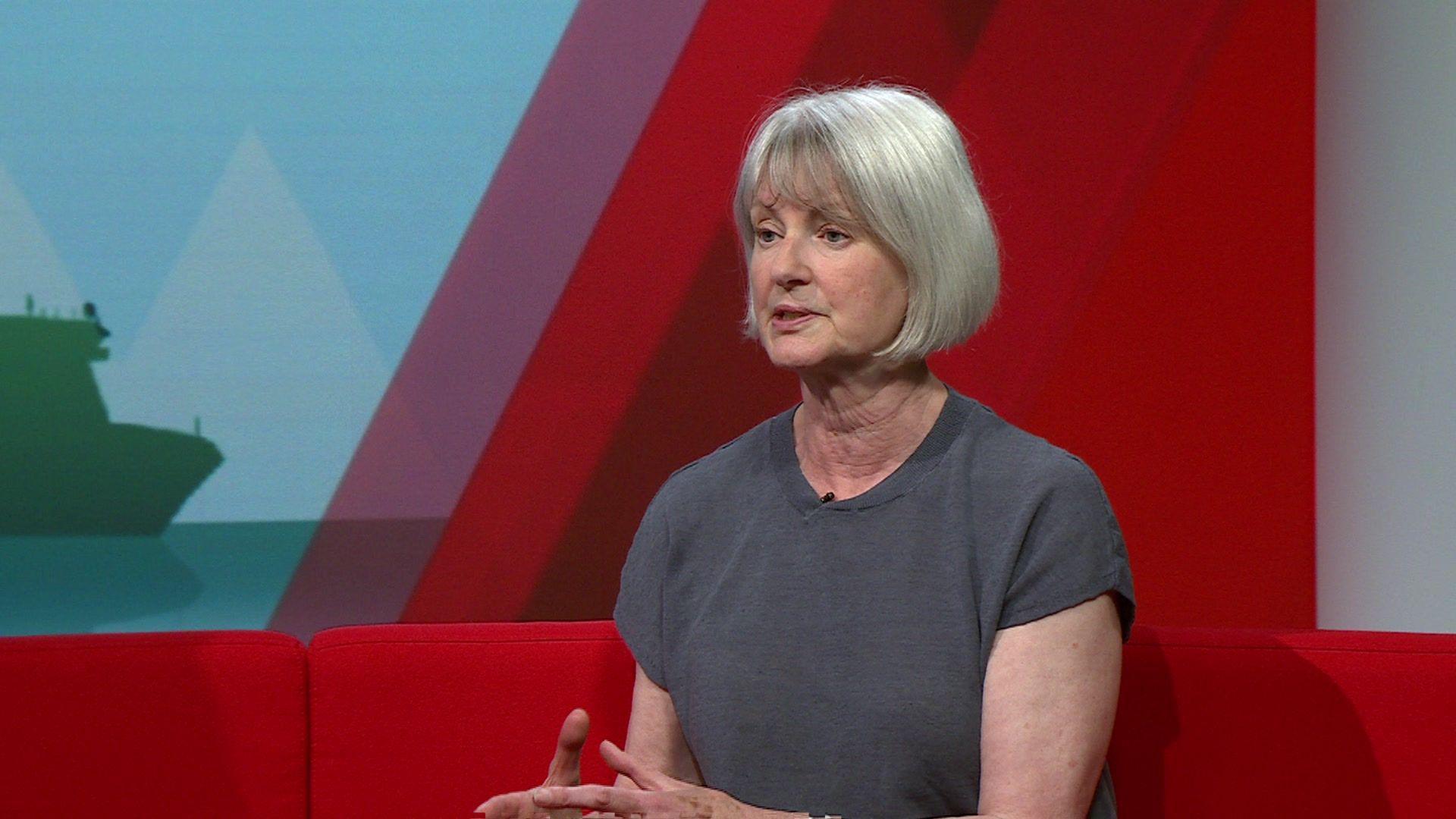 Liz Leffman talking to BBC Politics South. She is sitting on a red sofa looking away from the camera. She is wearing a grey sleeveless top