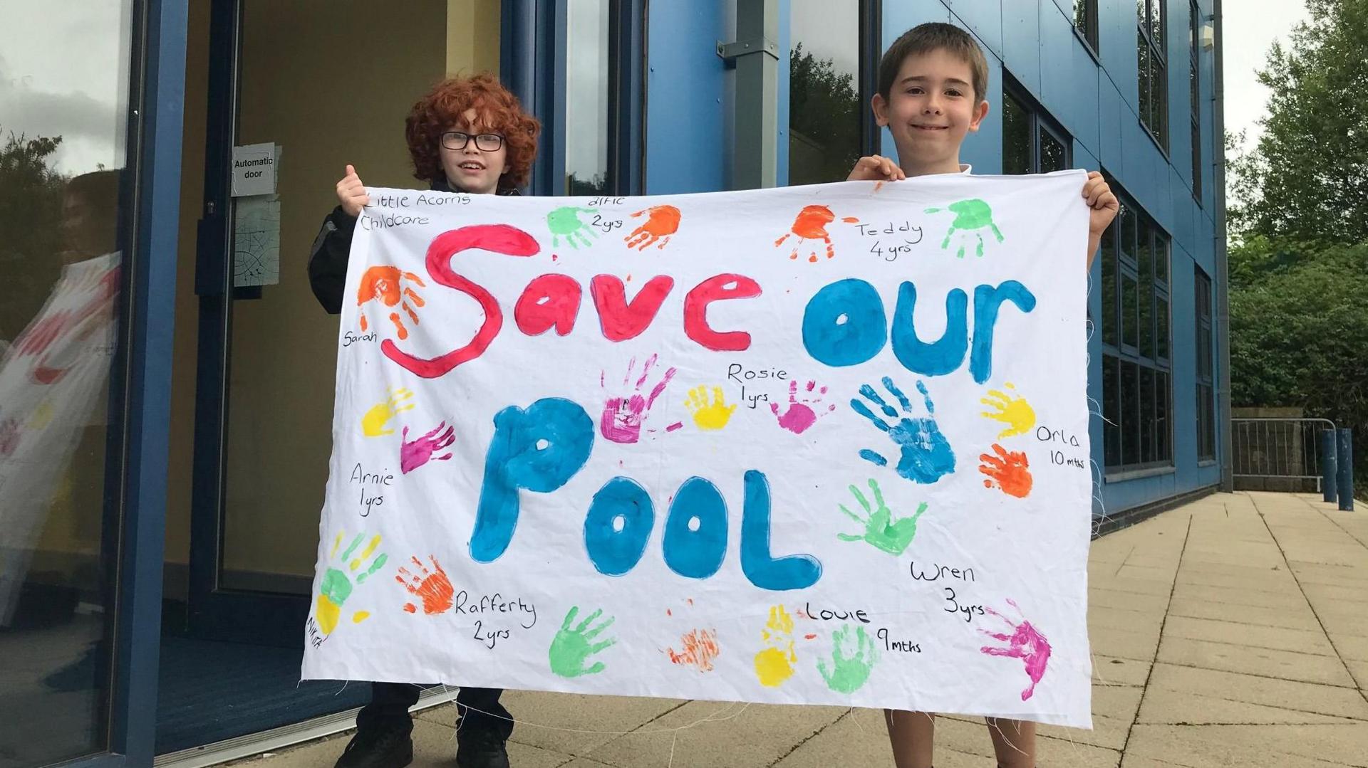 Two children hold up a 'Save Our Pool' sign