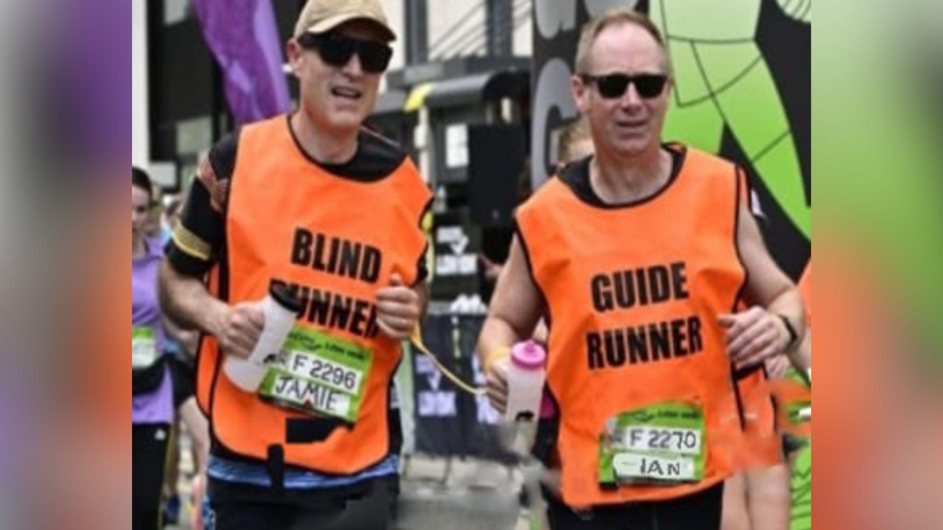 Two men wearing hi-vis orange vests running side by side each other.