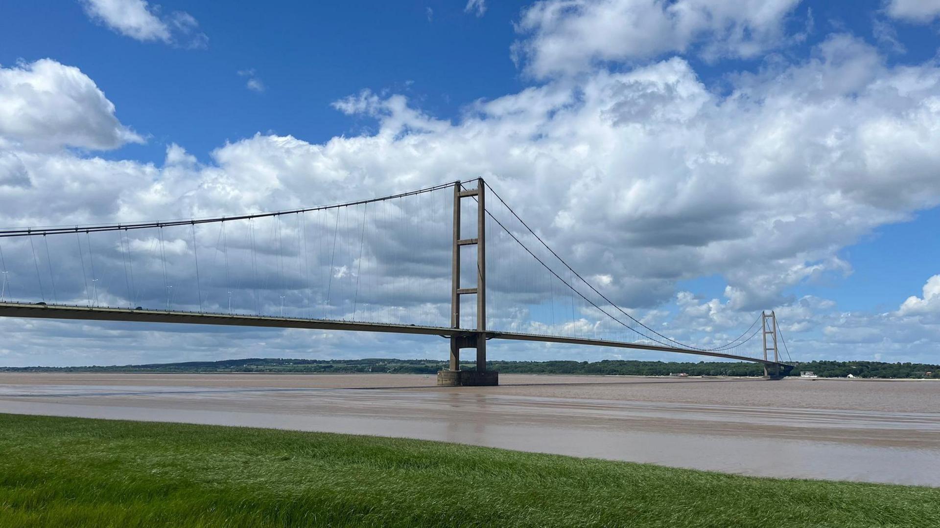 The Humber Bridge, stretching across the water on a sunny day with nimbus clouds overhead.