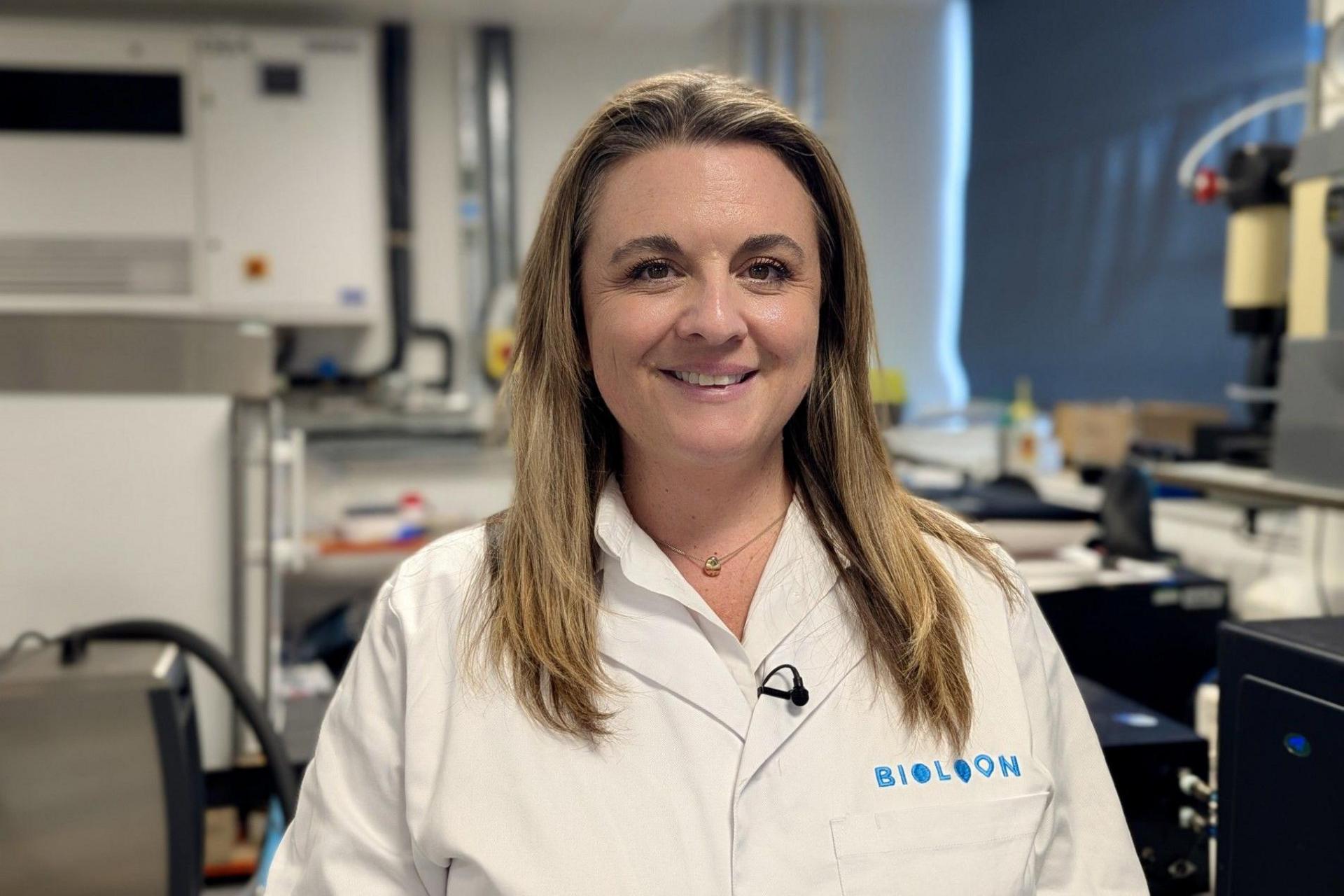 A woman in a lab coat smiles at the camera