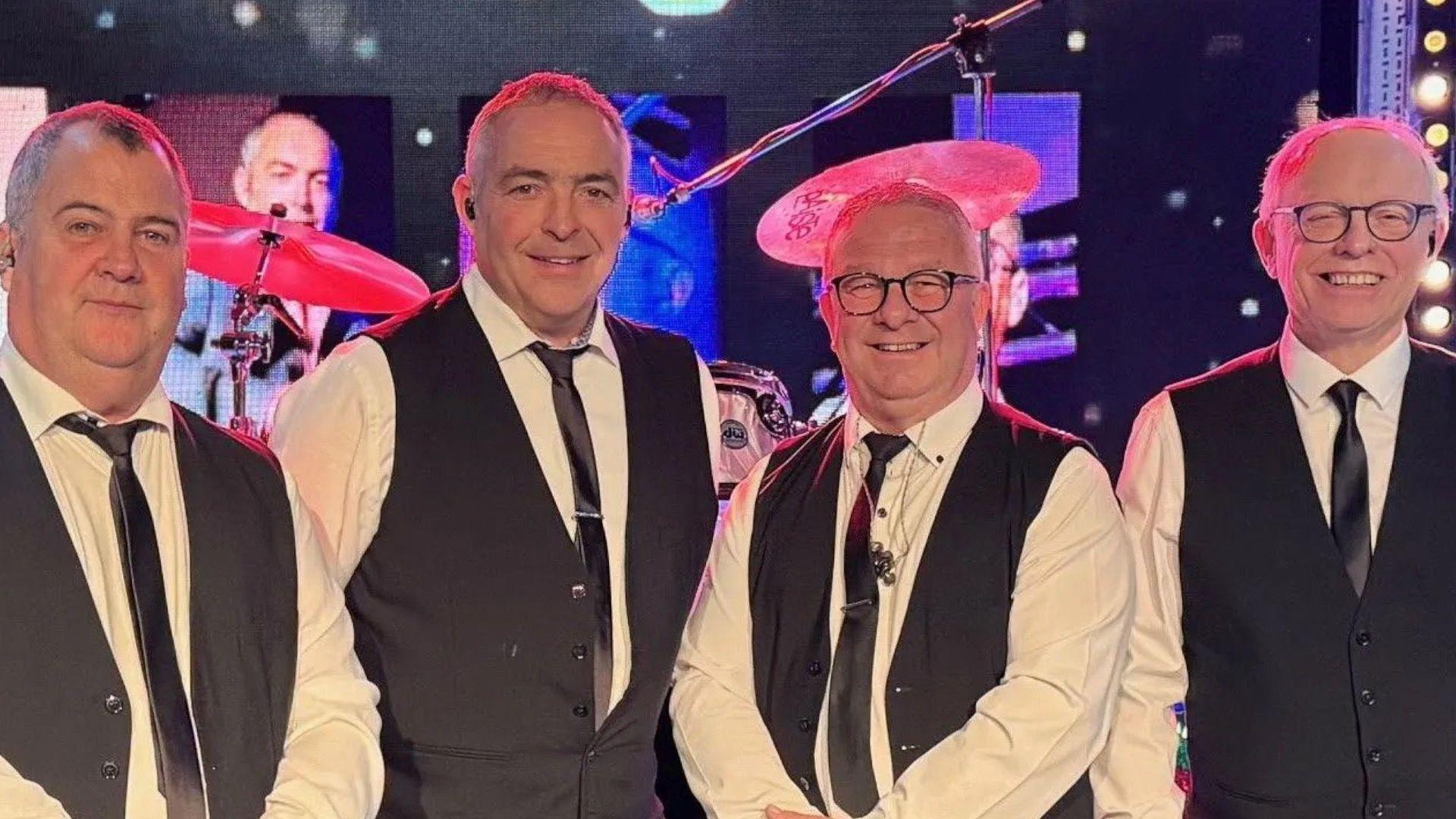 Four men in waistcoats and ties smiling at the camera.