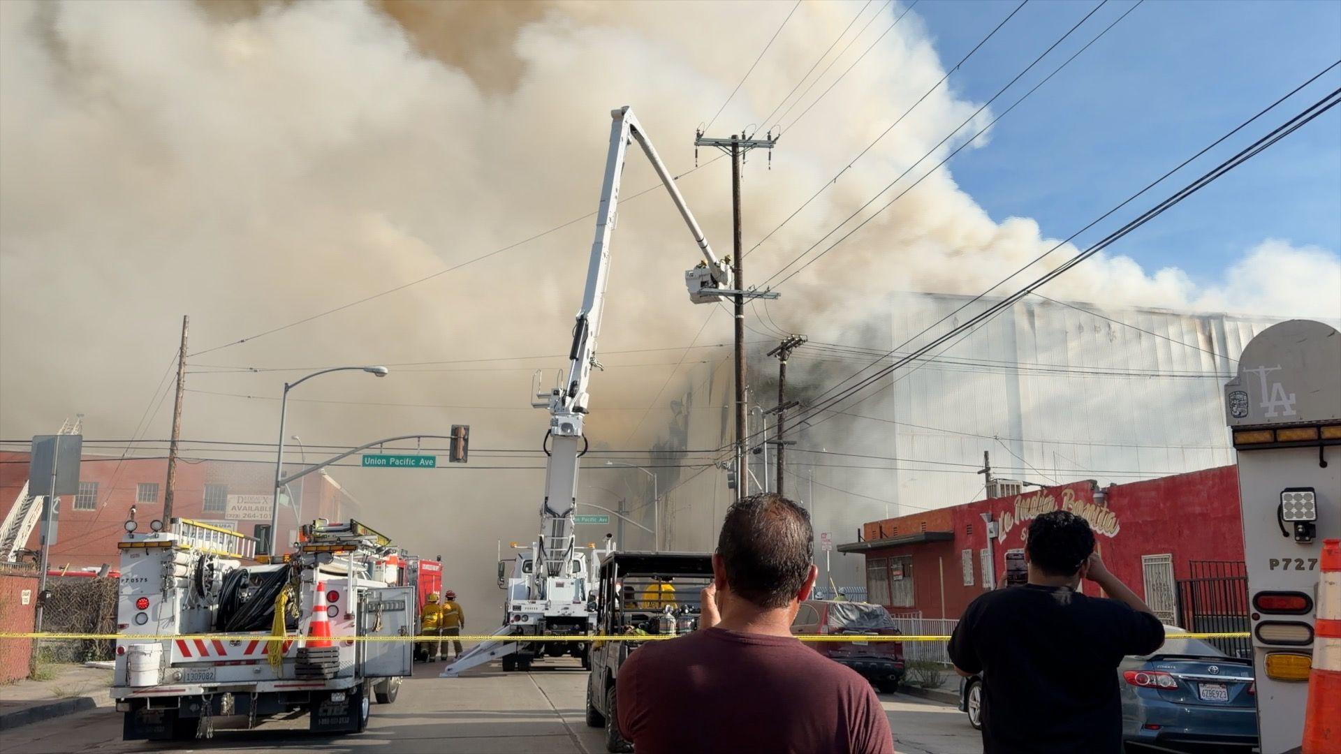 Smoke can be seen coming from a warehouse with spectators looking.
