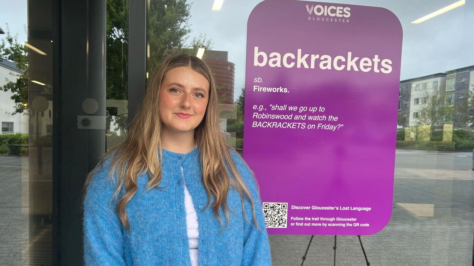 Girl stood in front of a window with a sticker on it that says, 'backrackets' and the definition which is 'fireworks'.