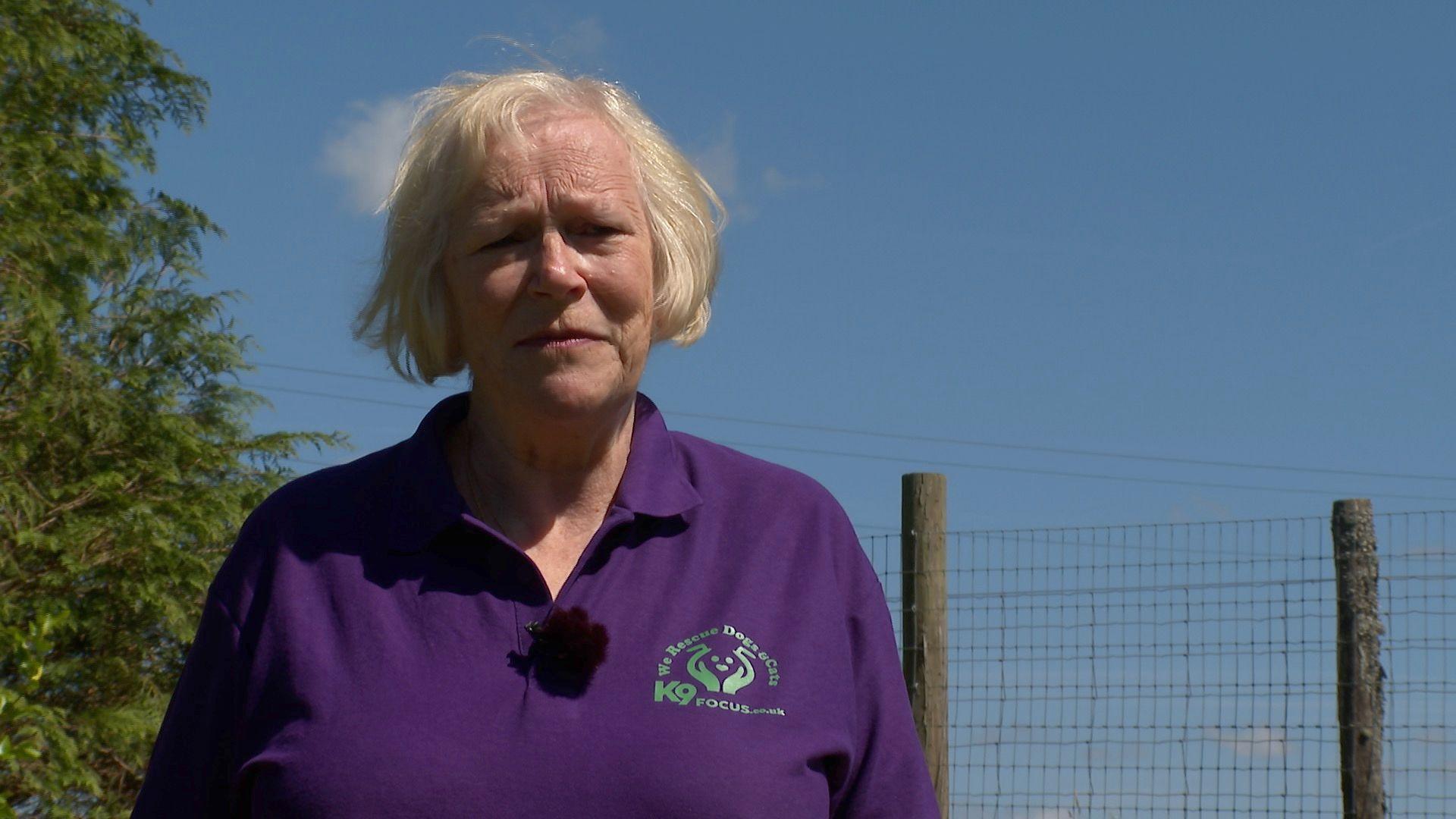 Lynne Hall, trustee of K9Focus dog and cat rescue charity in North Devon, standing outside, wearing a purple branded top.