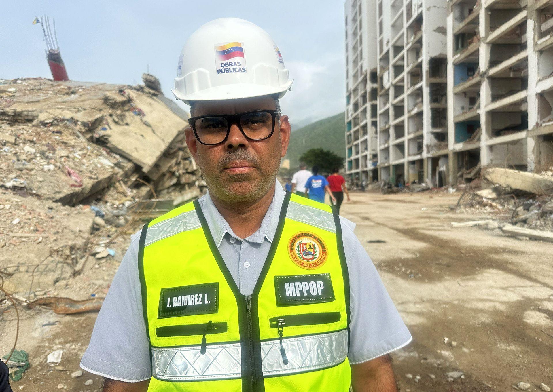 Public Works Minister Juan José Ramírez, wearing a high-visibility vest, a hard hat and glasses, looks into the camera while standing in front of rubble from a collapsed building.
