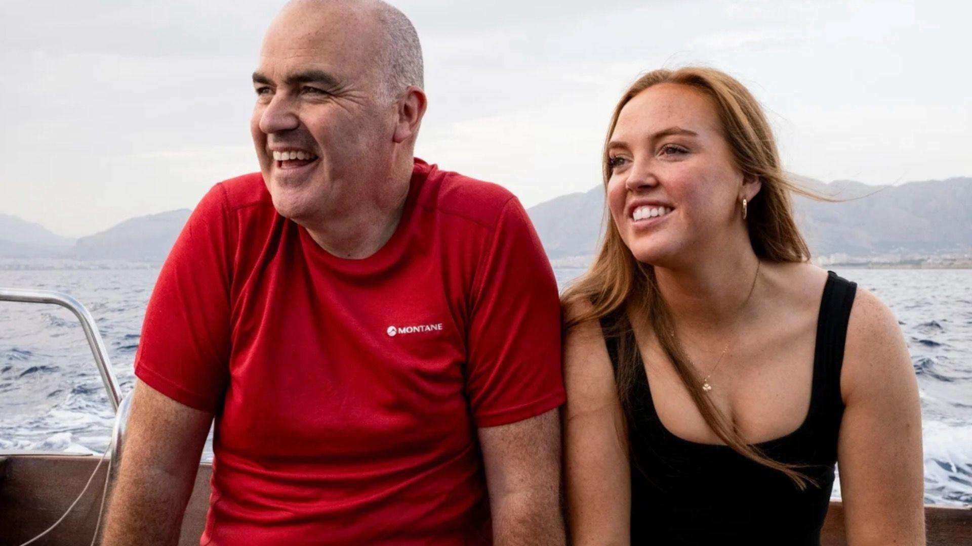 një burrë dhe një grua në një varkë, me male në sfond