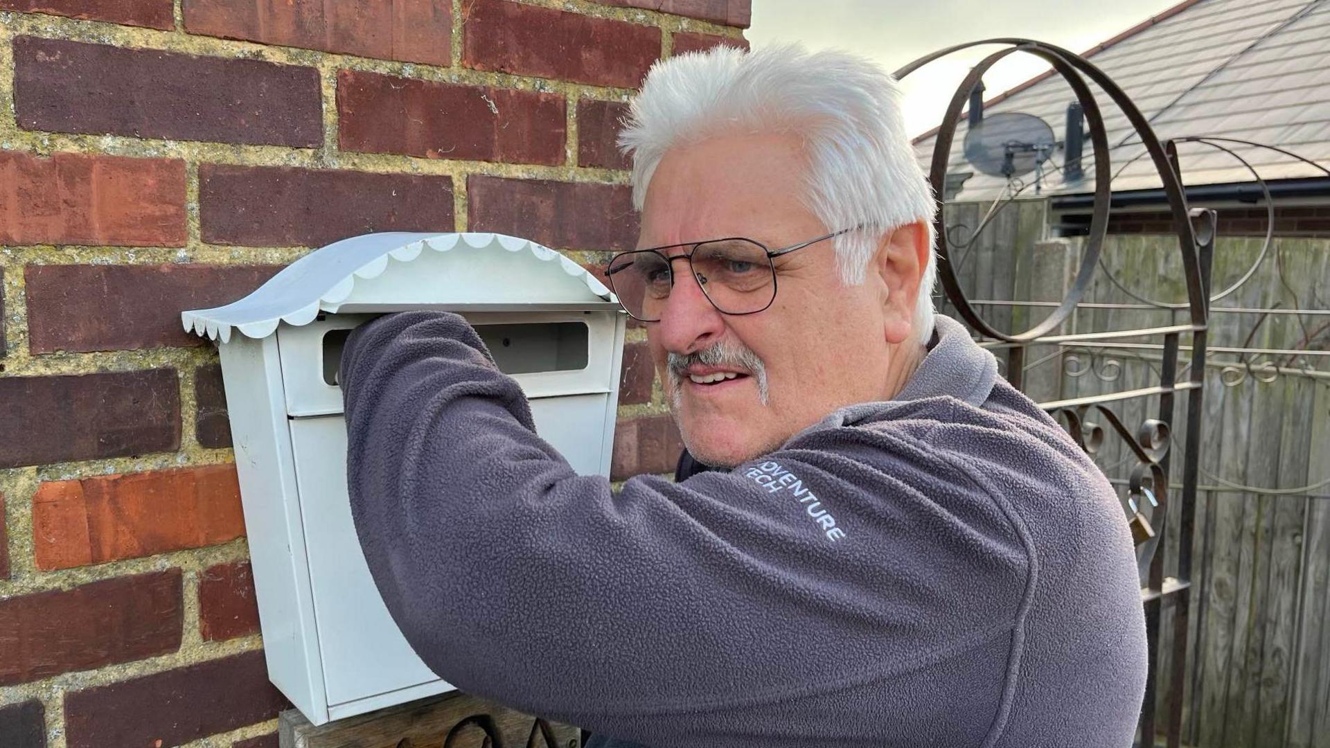 Gary Westwick reaches into the mailbox outside his home on Chequer Lane, Ash, with a disappointed look on his face