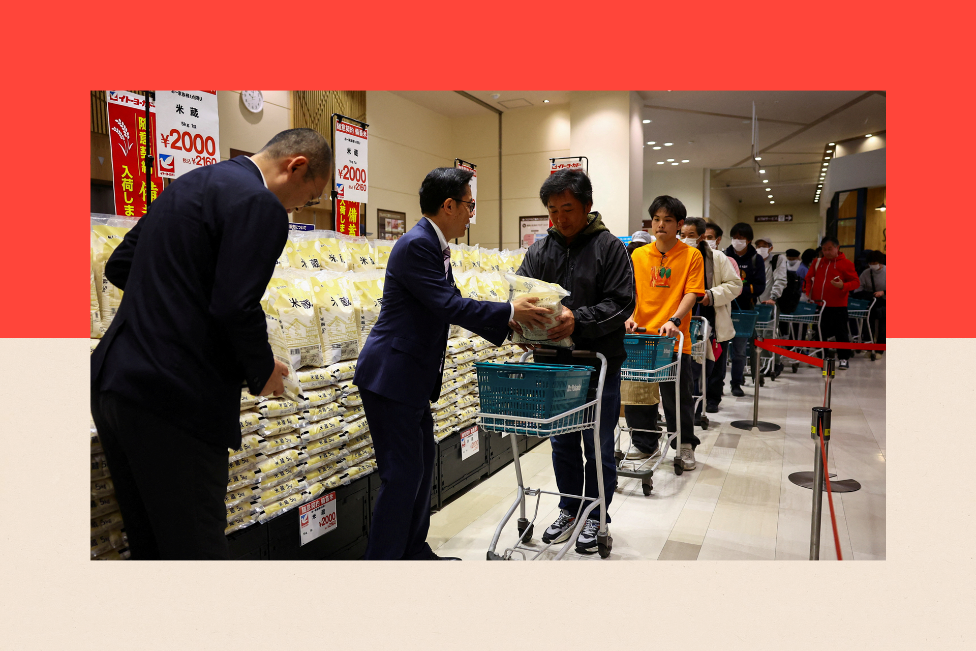 People stand in line with shopping trolleys to buy rice while men in suits hand it out