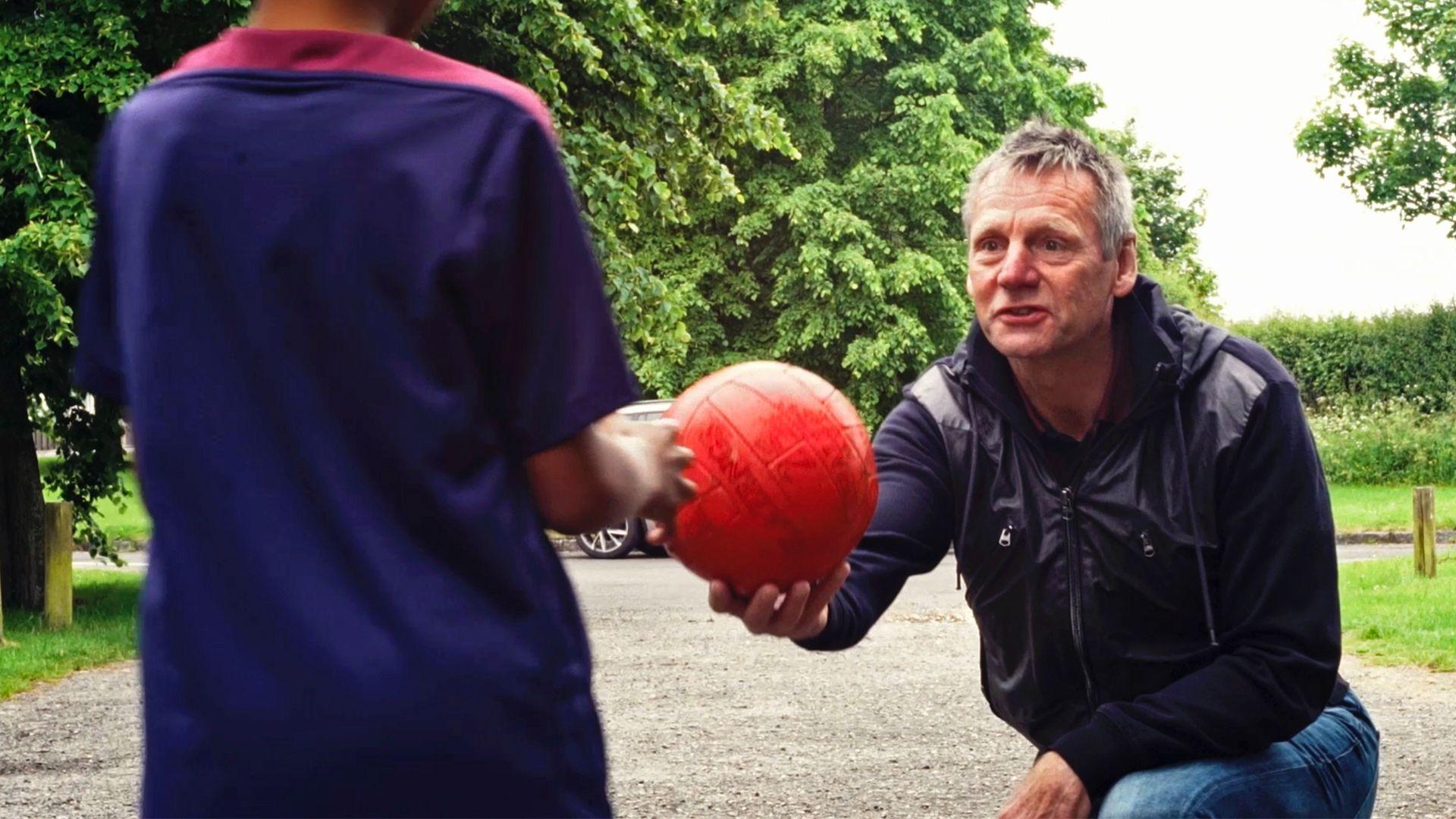 Stuart Pearce handing a red football to a boy wearing an England strip