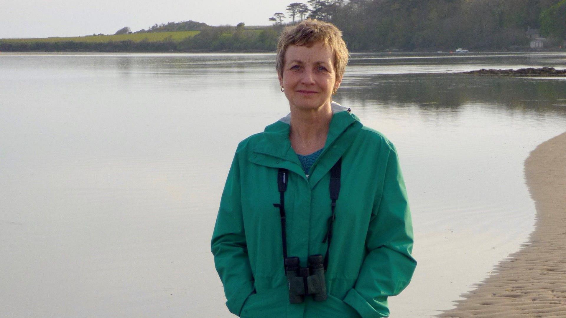 Mary Colwell standing in front of a body of water with binoculars around her neck