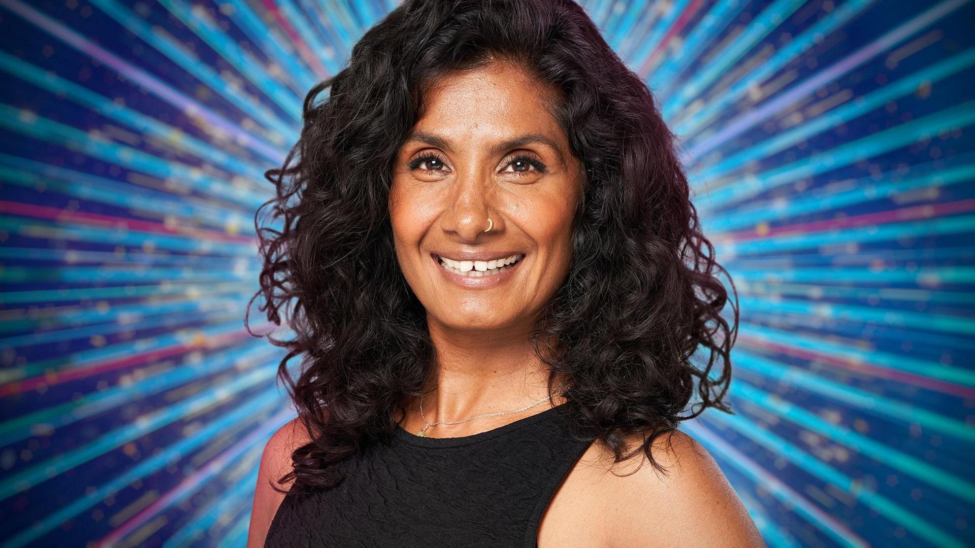 Close up image of a smiing Balvinder Sopal with a kaleidoscope background predominately blue