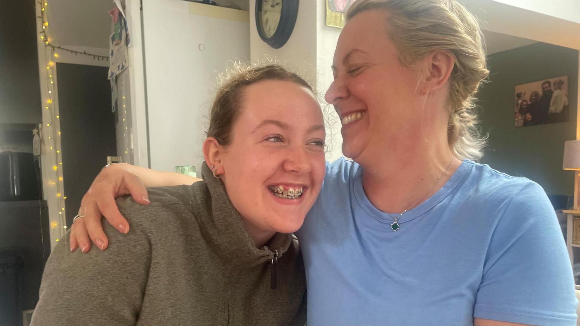 A young girl and an older woman laugh as they embrace