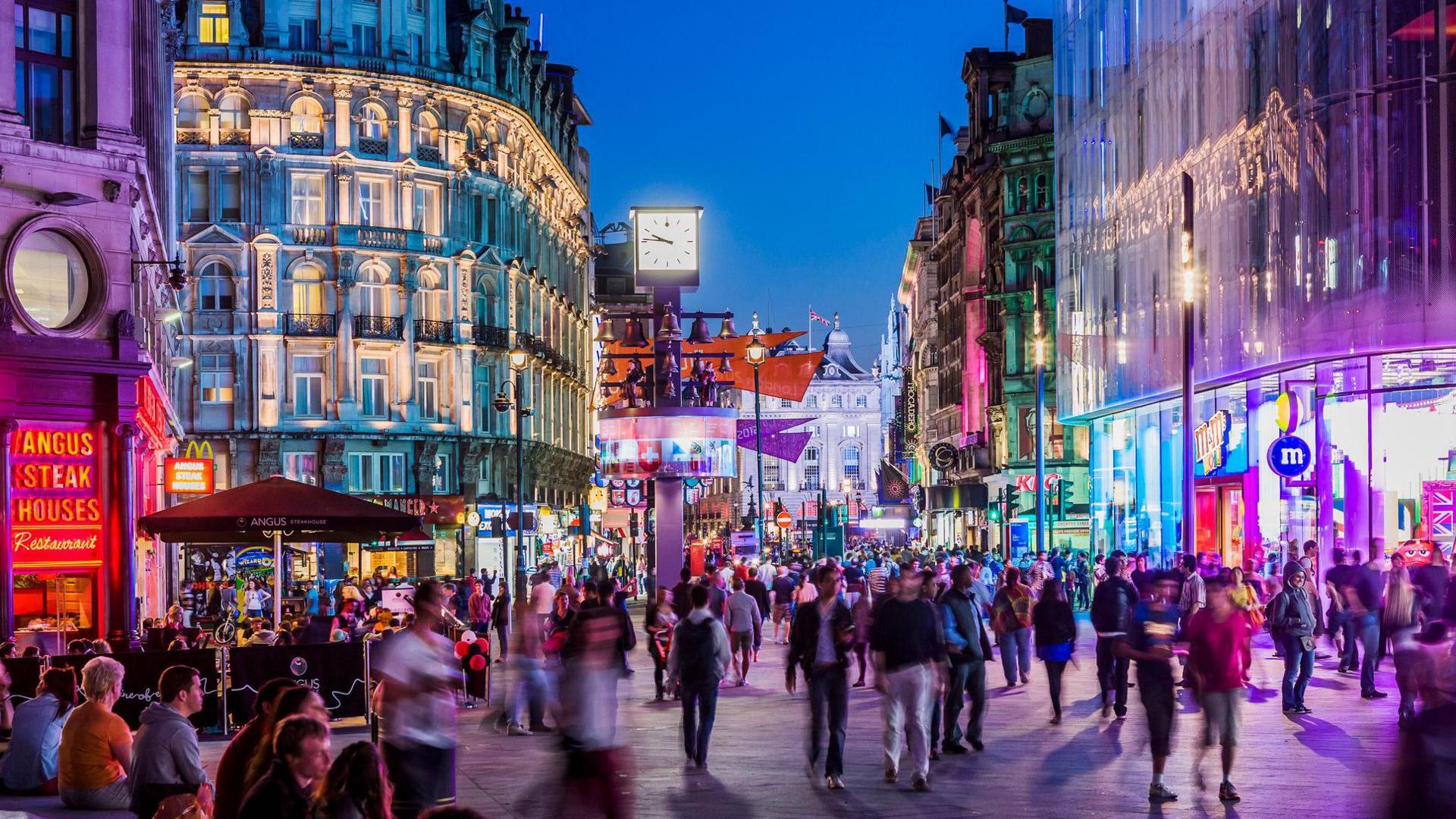 An artistic photo of Leicester Square at night with hundreds of people on the streets. 