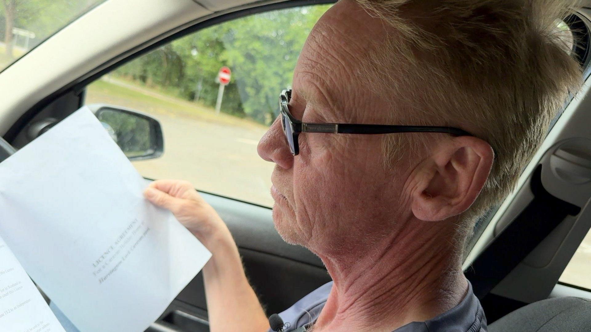 A man sits in his car looking at a paper document. 