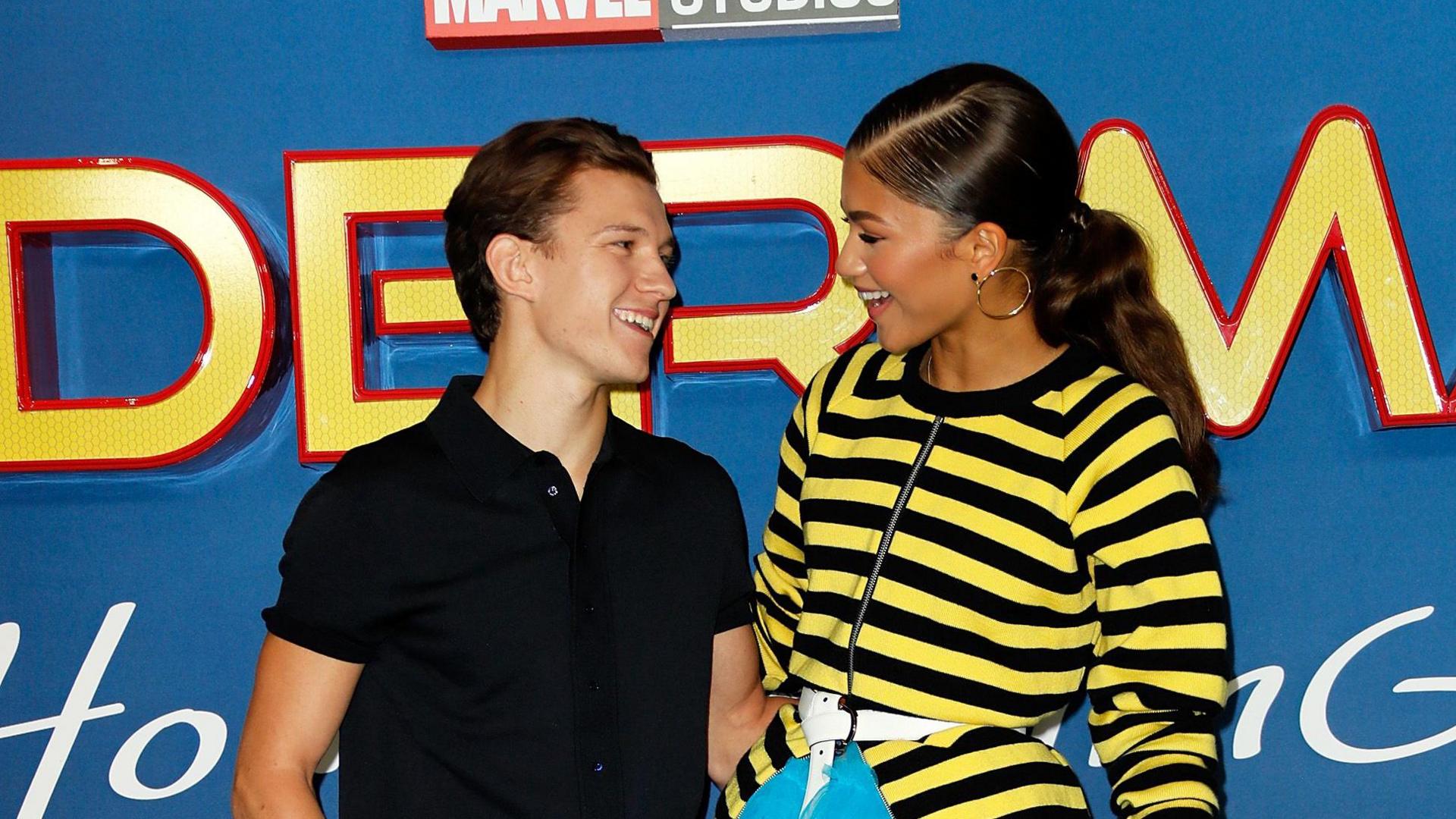 Tom Holland and Zendaya at the premiere for Spider-Man: Homecoming in 2017. Holland is wearing a black polo shirt and Zendaya is wearing a yellow and black striped top.