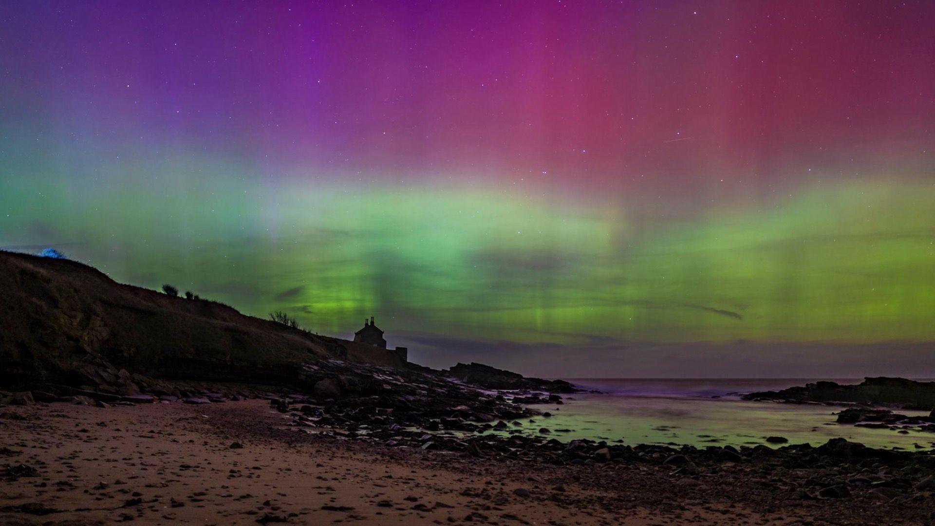 Purple and green skies swirl above an empty beach.