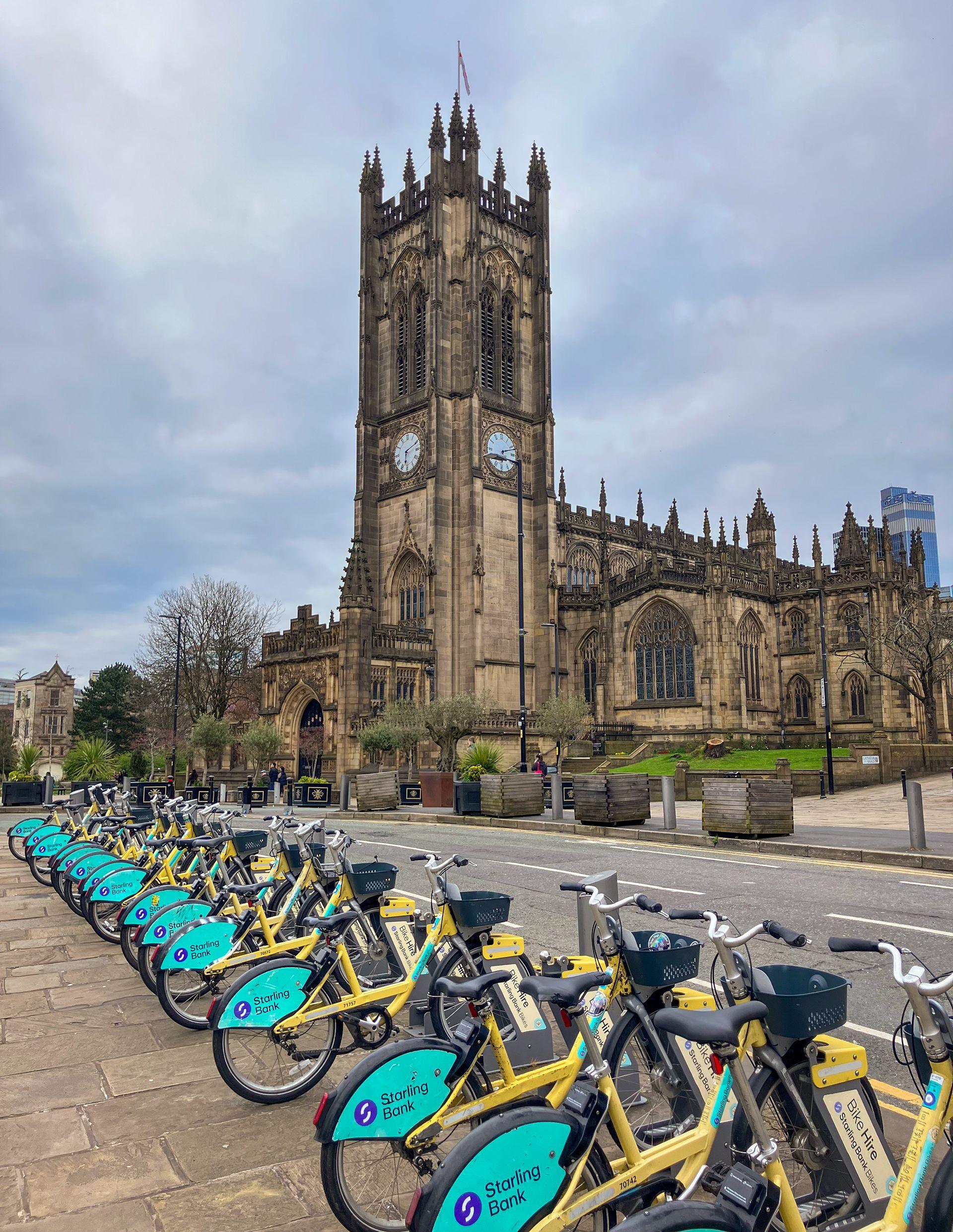 Rows of Starling Bank Bikes at a docking station in front of Manchester cathedral.