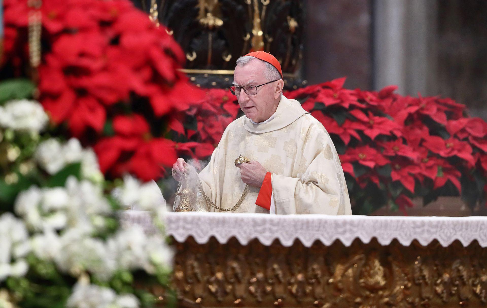 Cardinal Pietro Parolin wears a red cap on his head while he holds a smoking urn on a table against a backdrop of red chrysantheums during the Holy Mass on the occasion of the Solemnity of Mary, Mother of God, in St. Peters Basilica, Vatican City on 1 January.