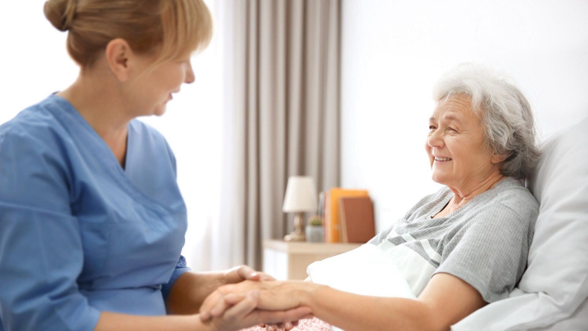 Woman caring for an elderly woman who is lying in a bed