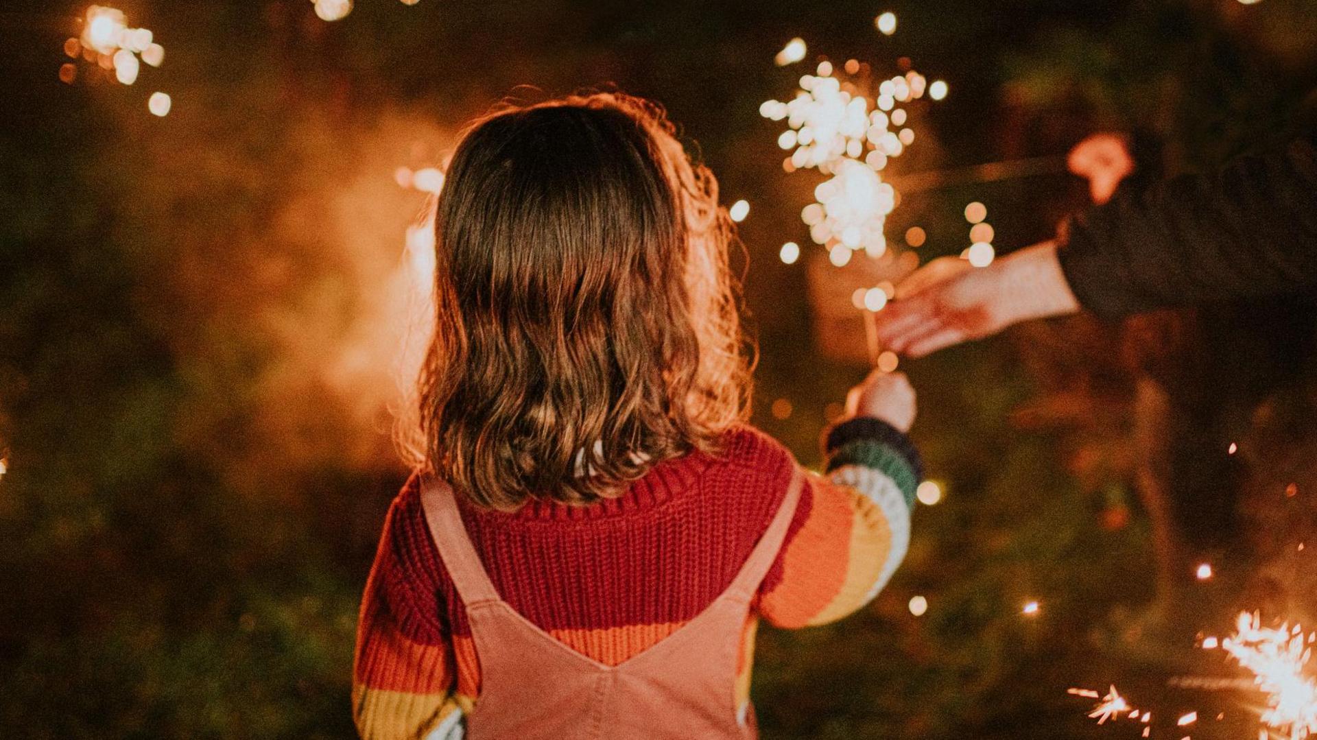 A child holds a sparkler in the darkness, surrounded by other burning sparklers.