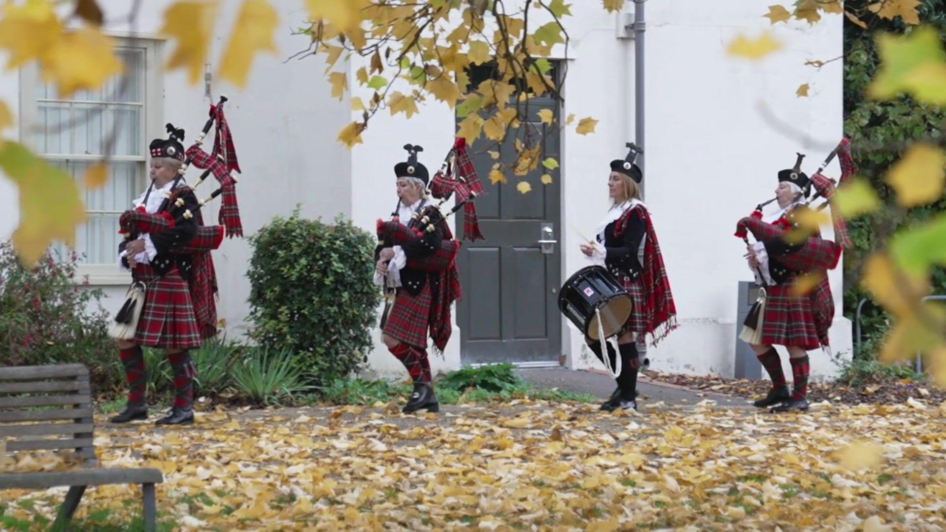 Sheila Hatcher and Denise Morrison stood outside in their uniforms, consisting of a black velvet jacket, red tartan bagpipes, a black drum, white lace collars and black hats 