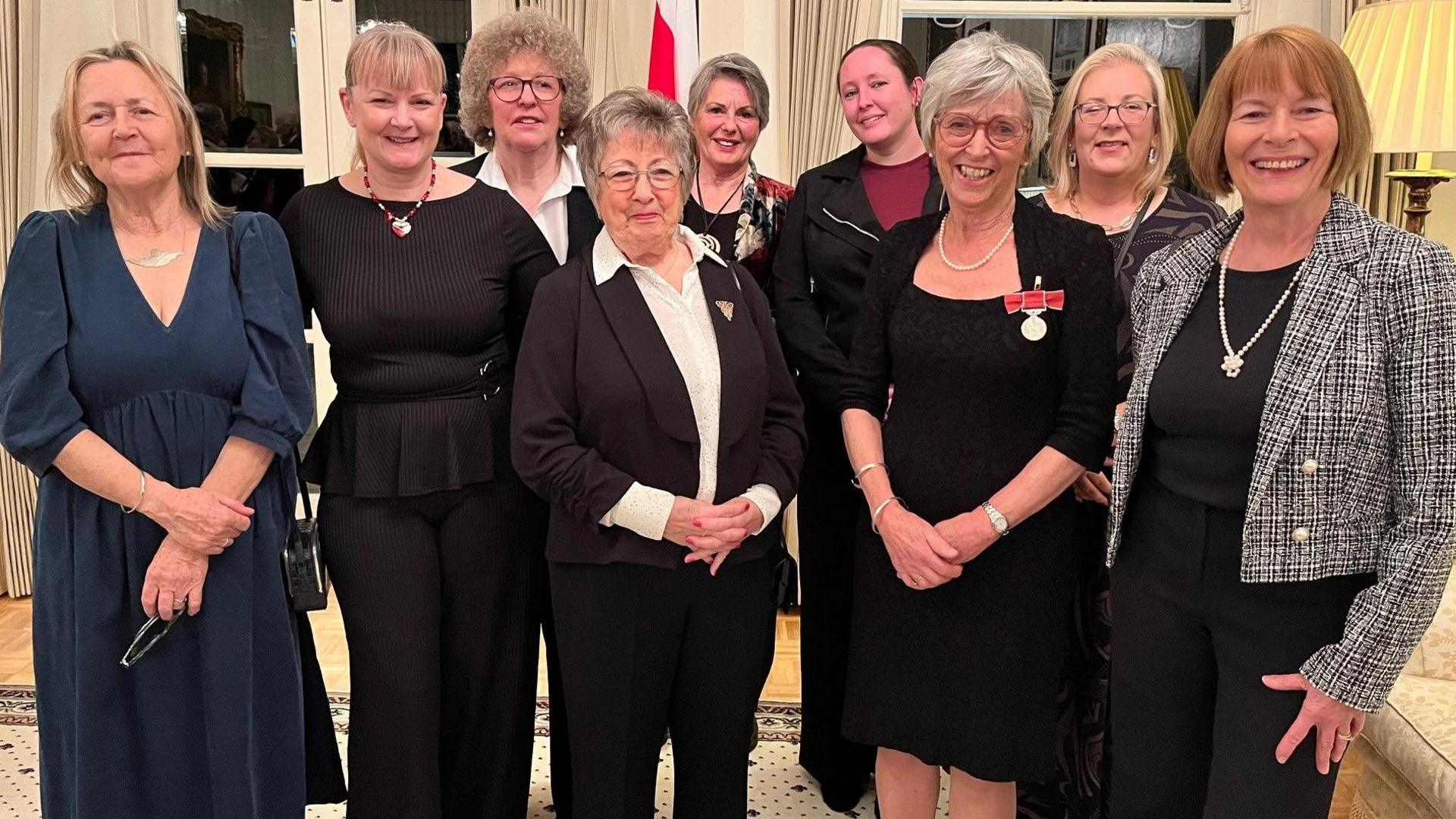 Marguerite Talmage is standing with a eight female colleagues from Welfare Animals Guernsey. She is wearing her medal and they are all smartly dressed and smiling. 