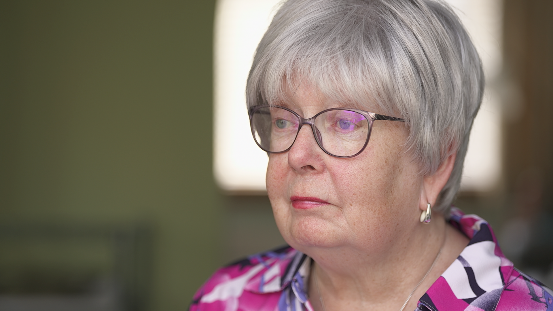 Marion Fellows, who has short grey hair and wears a colourful pink top, looks off camera as she speaks to the BBC.
