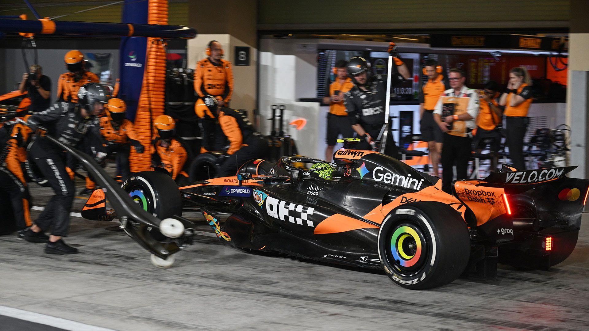 A Formula 1 car in a pit stop, with lots of staff wearing orange and black team outfits running around to help change the tyre