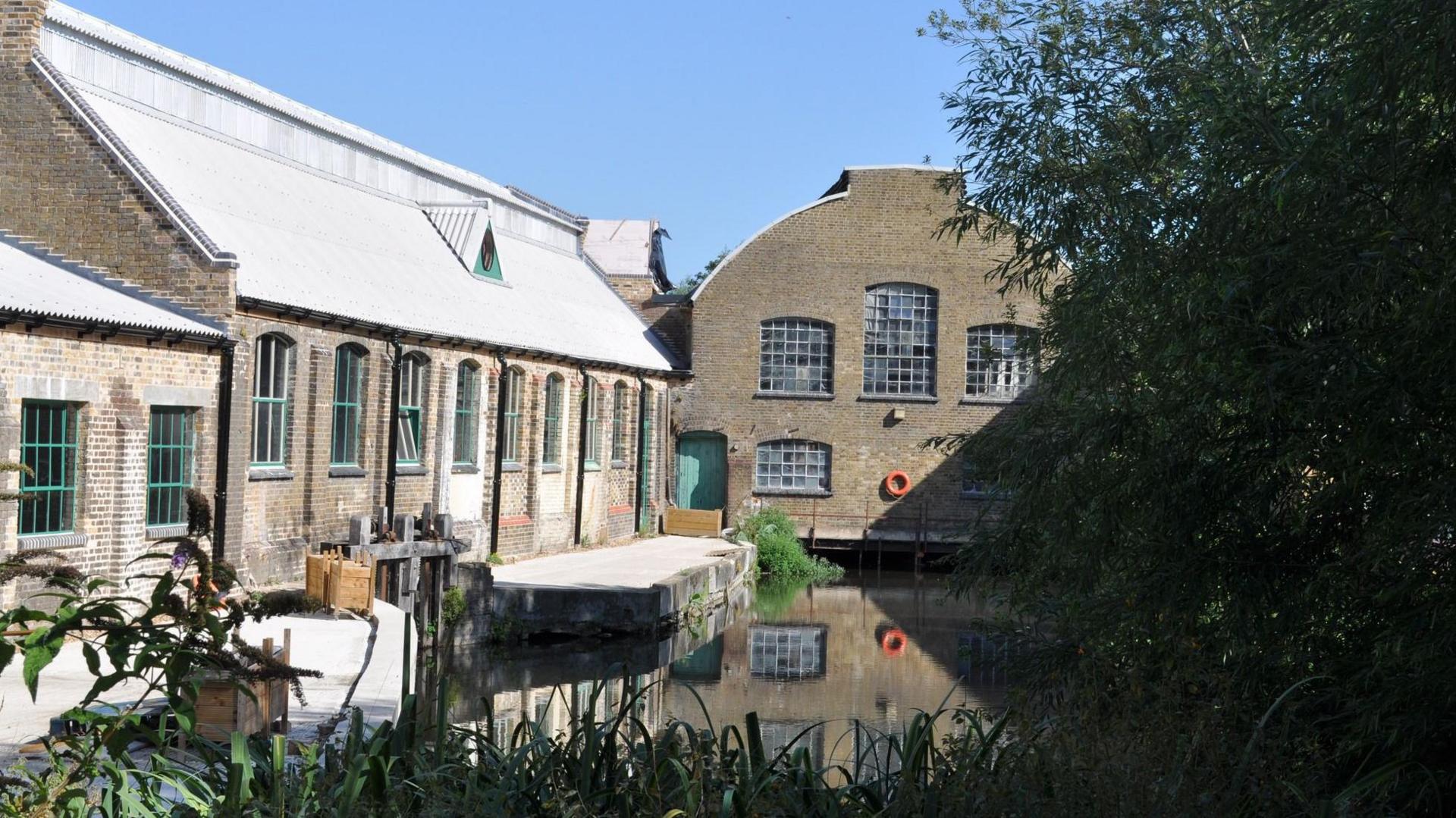 The exterior of Frogmore Paper Mill in Apsley, taken on a sunny day with the building reflecting in the water.