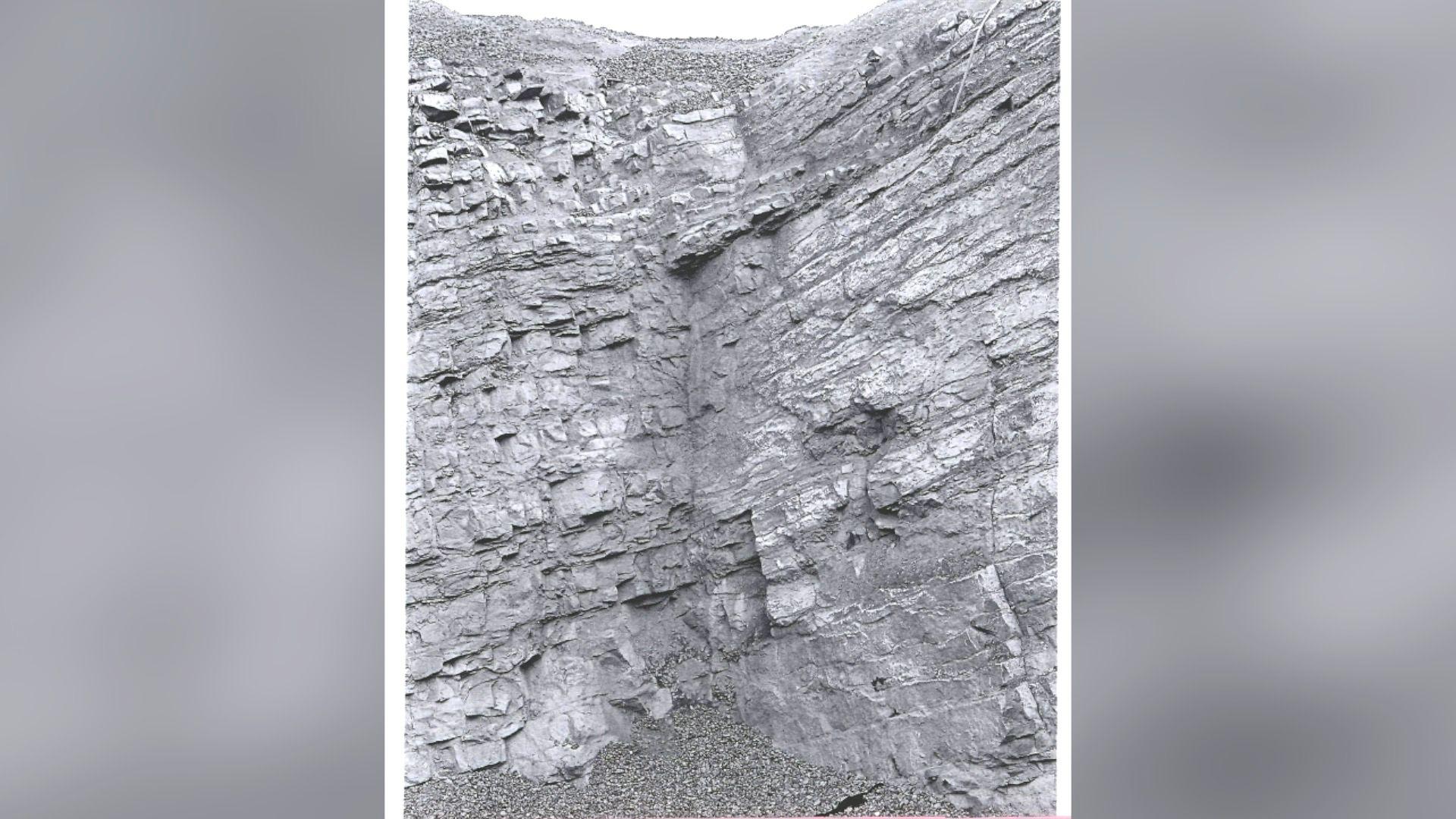 A black and white image of the inside of the quarry which is rocky and there are loose stones on the ground.