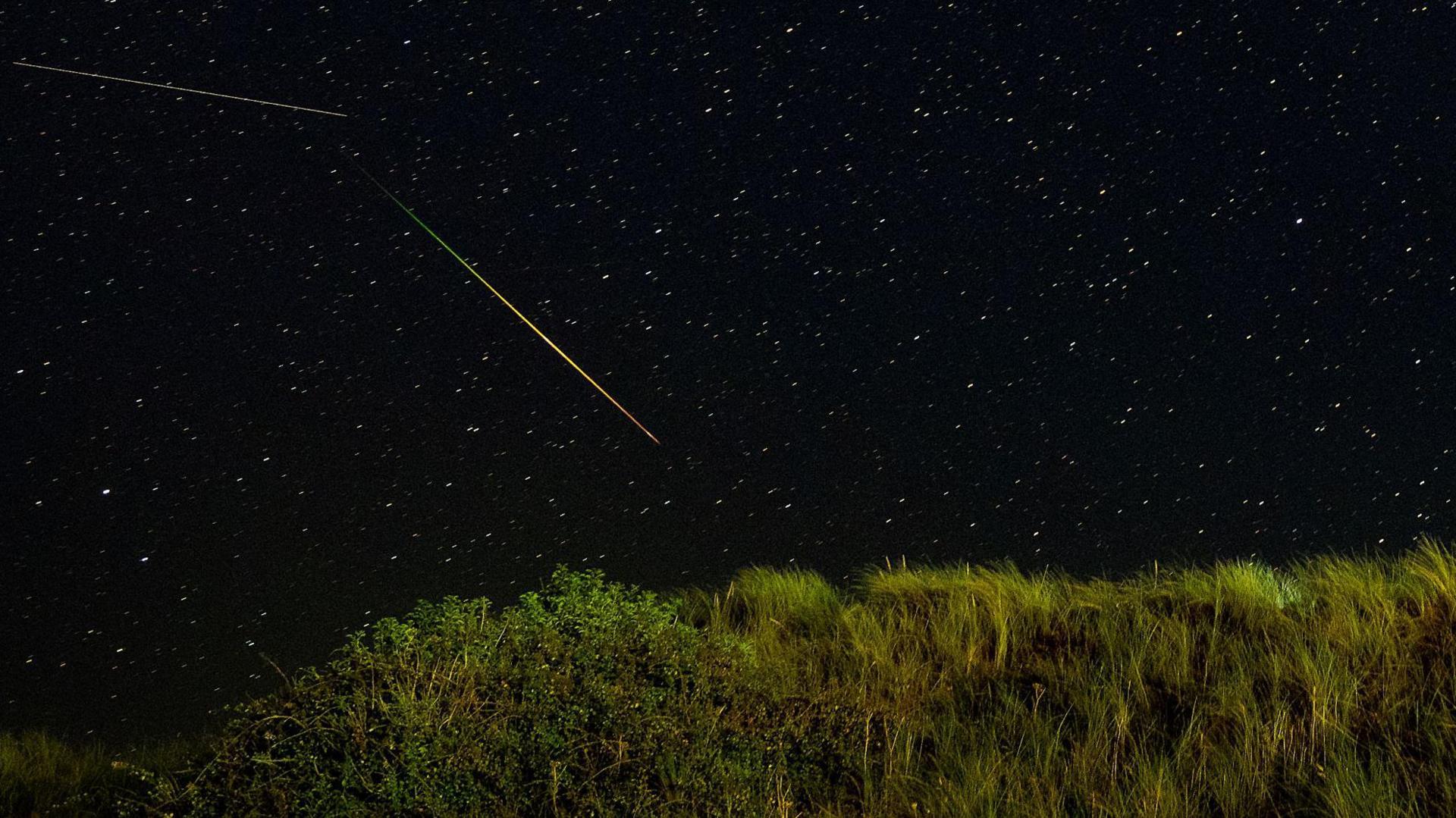 The Perseid meteor shower reveals dots (stars) in the sky and two long lines of light or shooting stars.