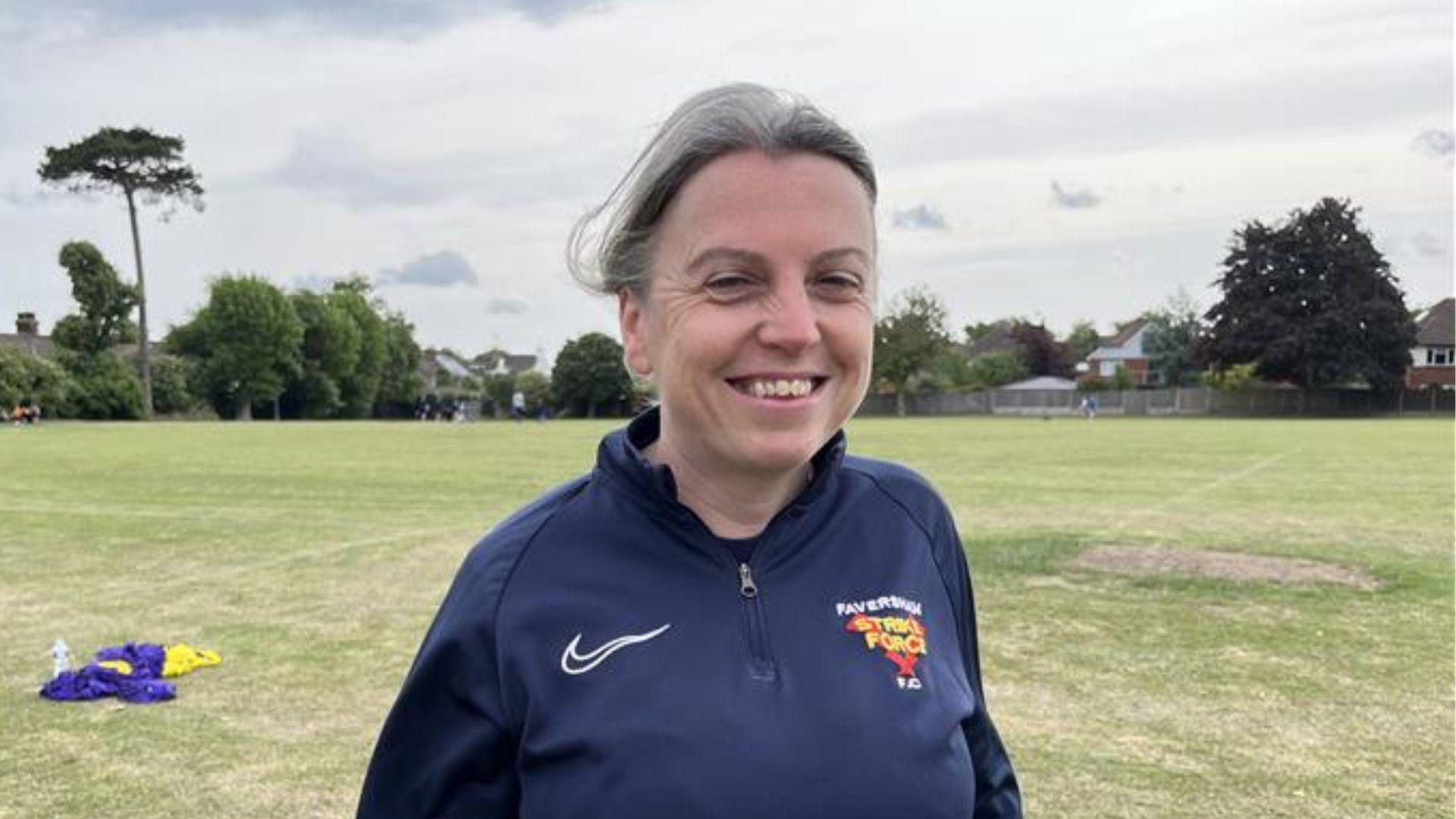 A woman wearing a navy blue coat smiling at the camera while stood in a field